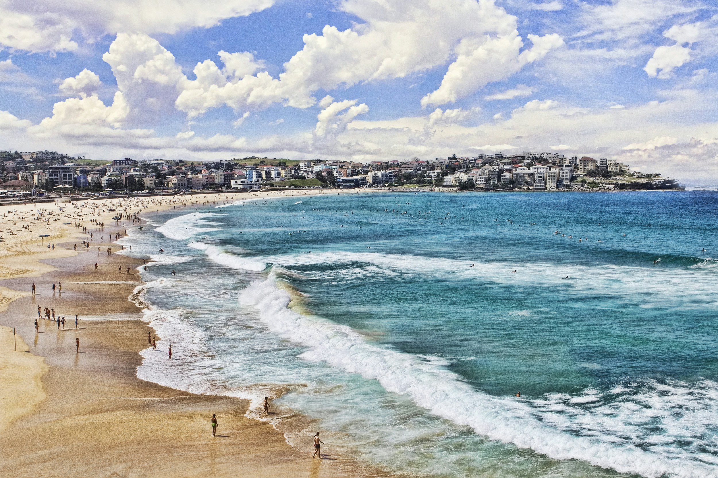 The curve of a large beach with waves crashing on the shore and people on the sand