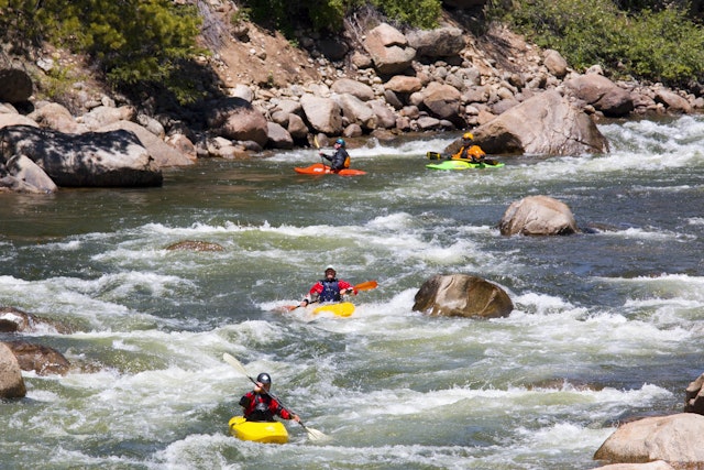 People in small kayaks paddle down a river