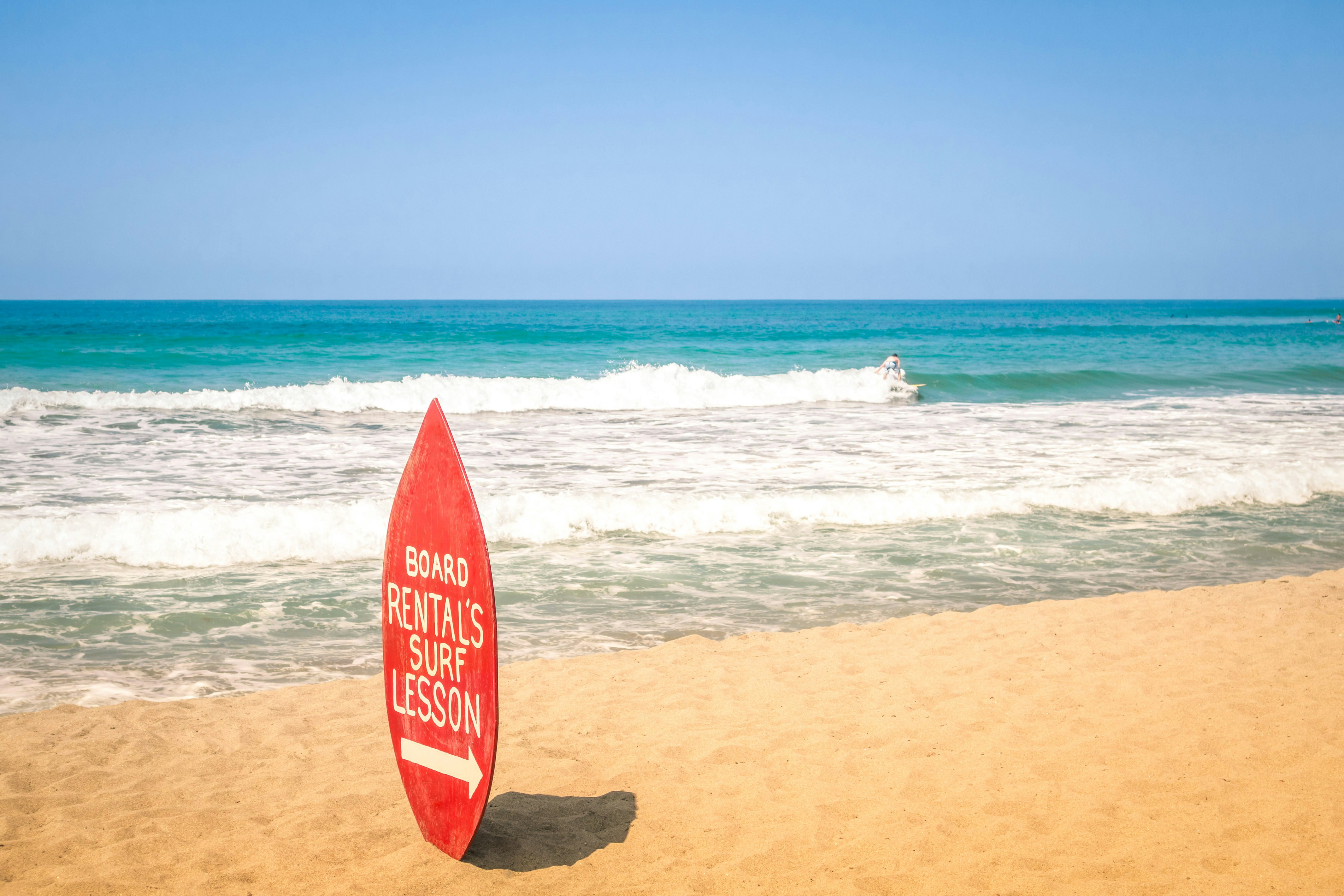 Surfboard rental and surf lesson sign on a sandy beach