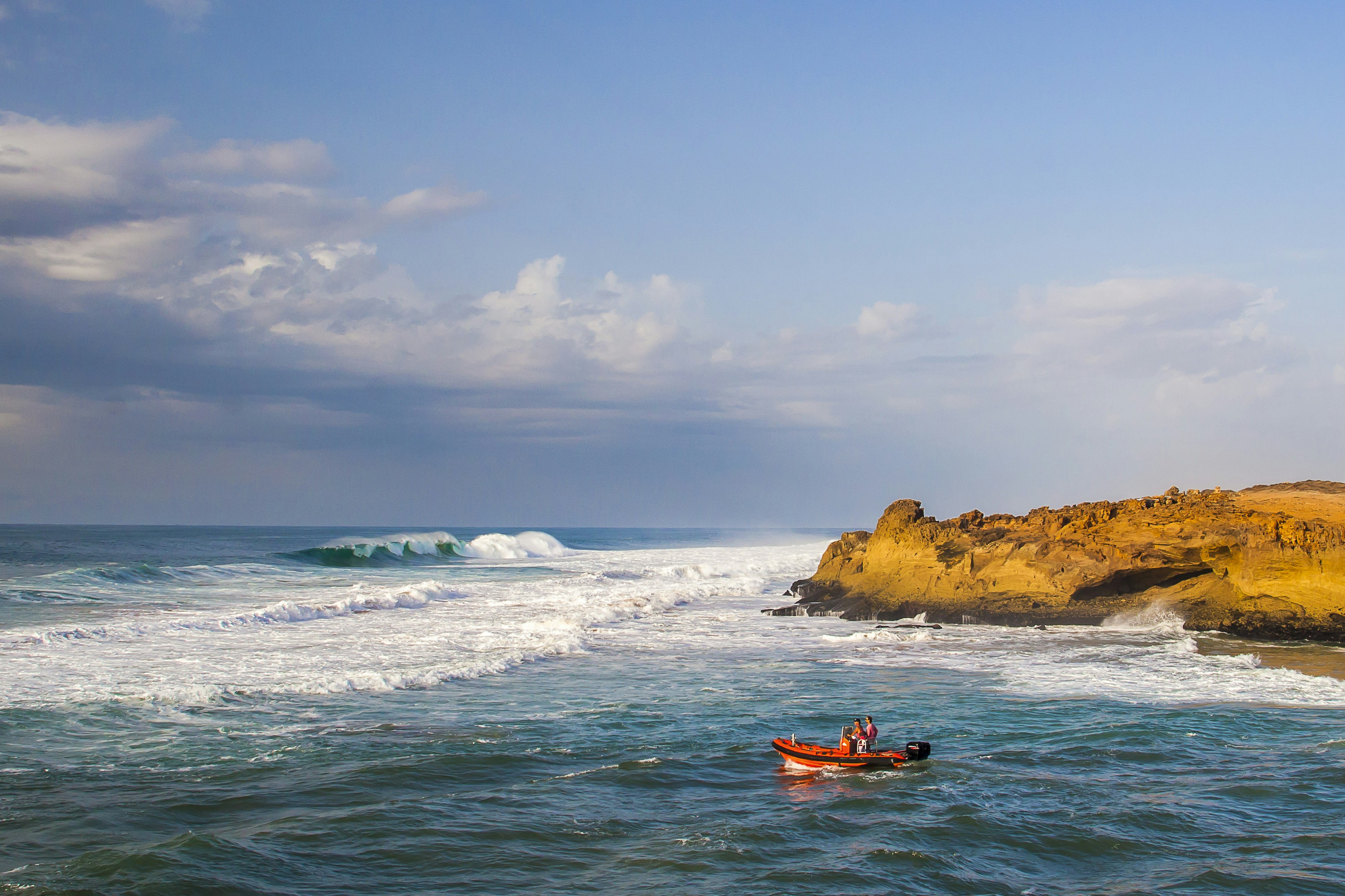 Two men in a red motorboat head out to the surf at Oualidia beach