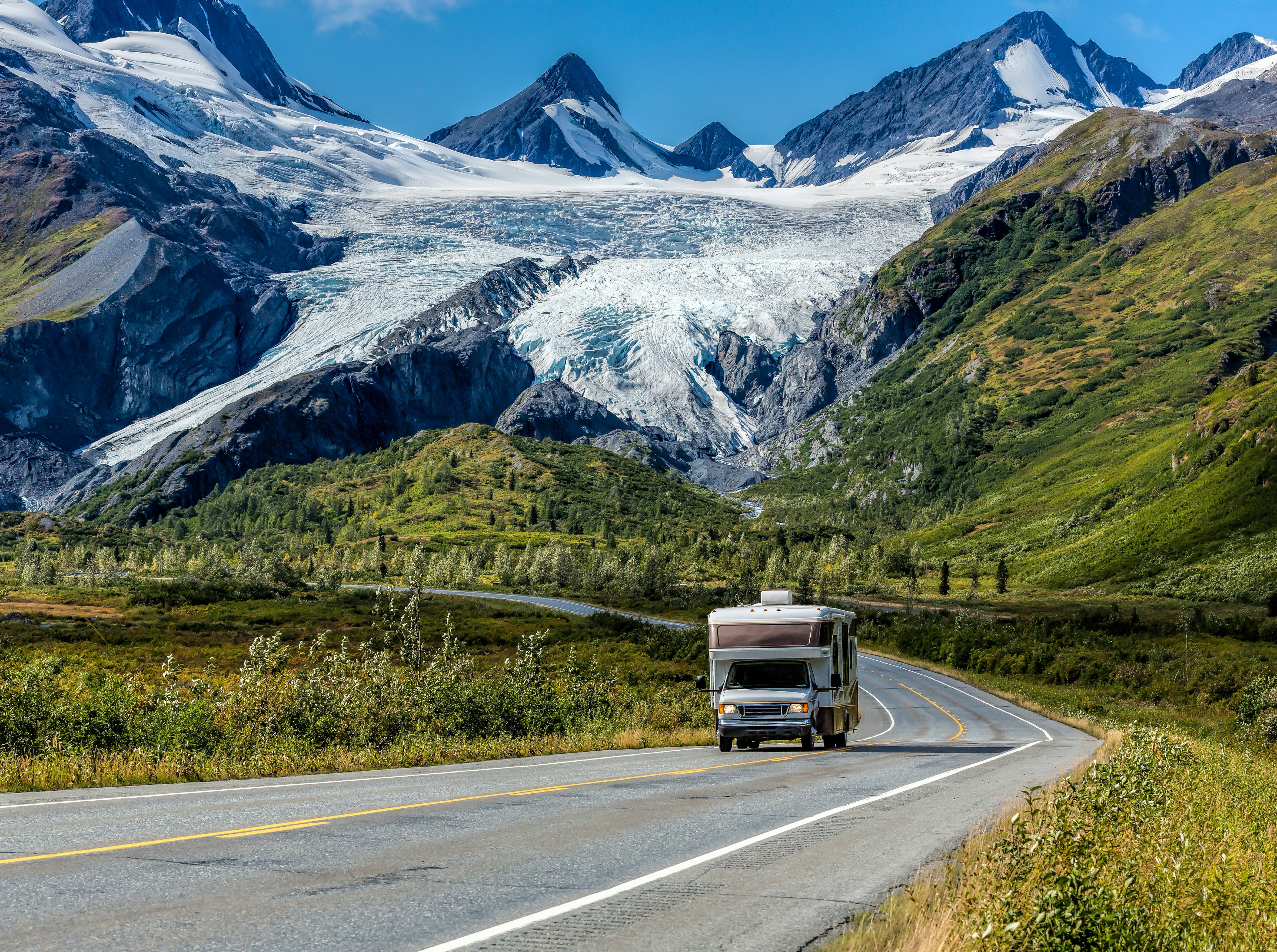 An RV driving on the Richardson Highway in Alaska with a glacier and mountains in the background