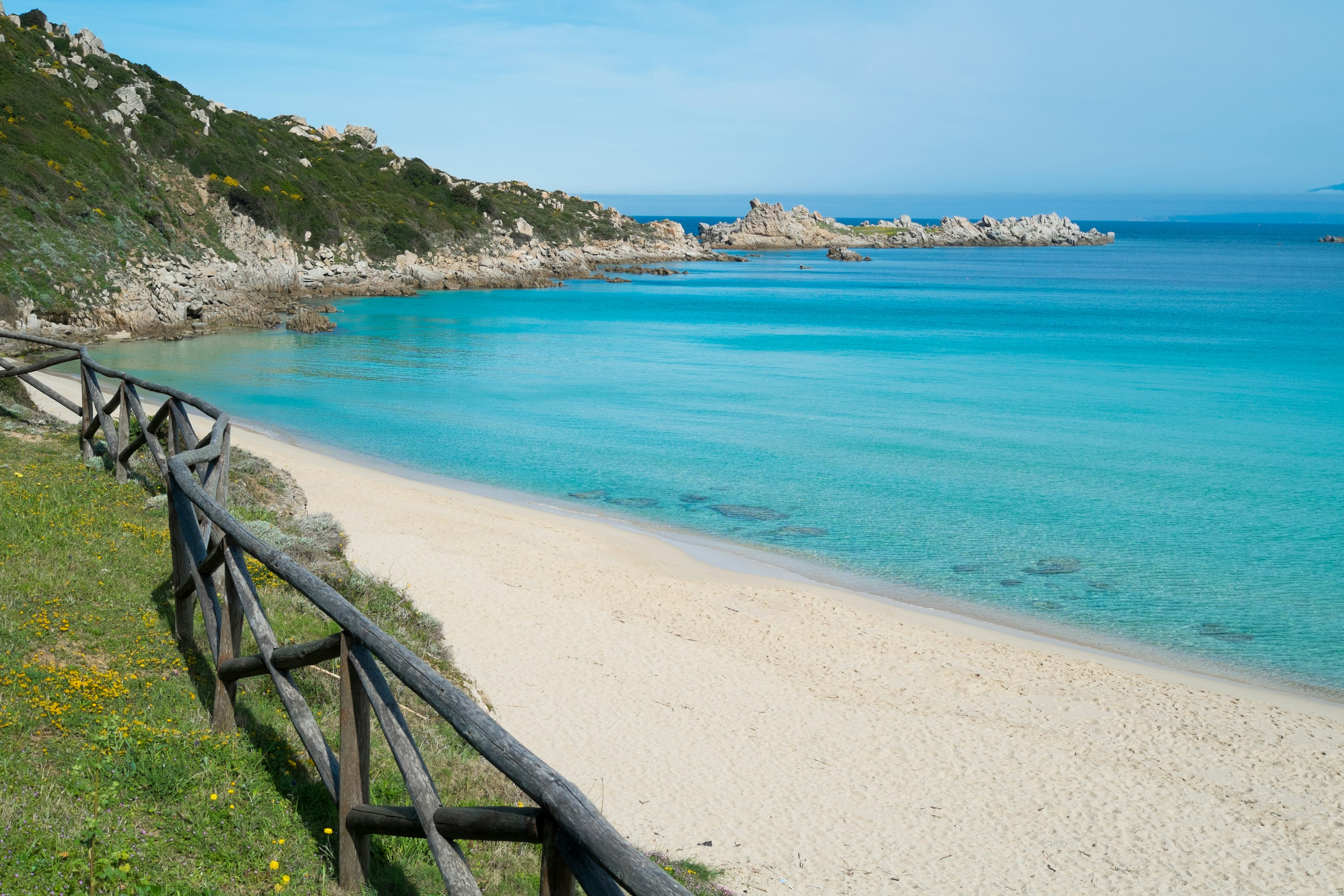 A wooden gate runs along side the sand on Spiaggia Rena Bianca in Sardinia.