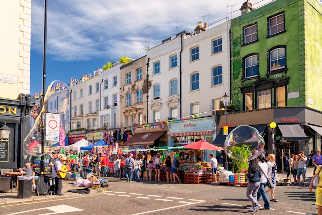 A row of pastel-colored houses on a street lined with shops and busy with people