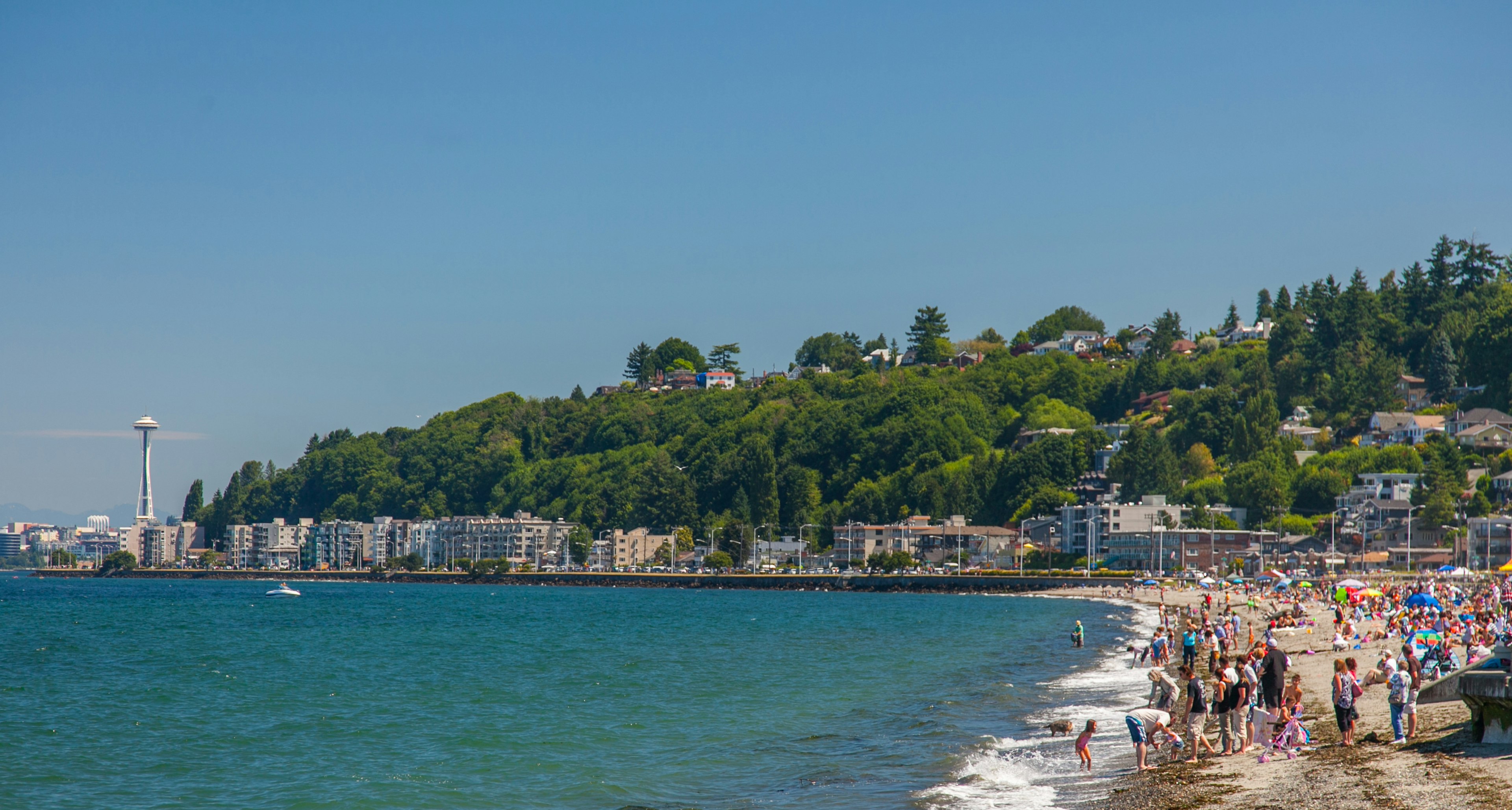 Sunbathers and beach-goers enjoy a sunny day at Alki Beach in Seattle