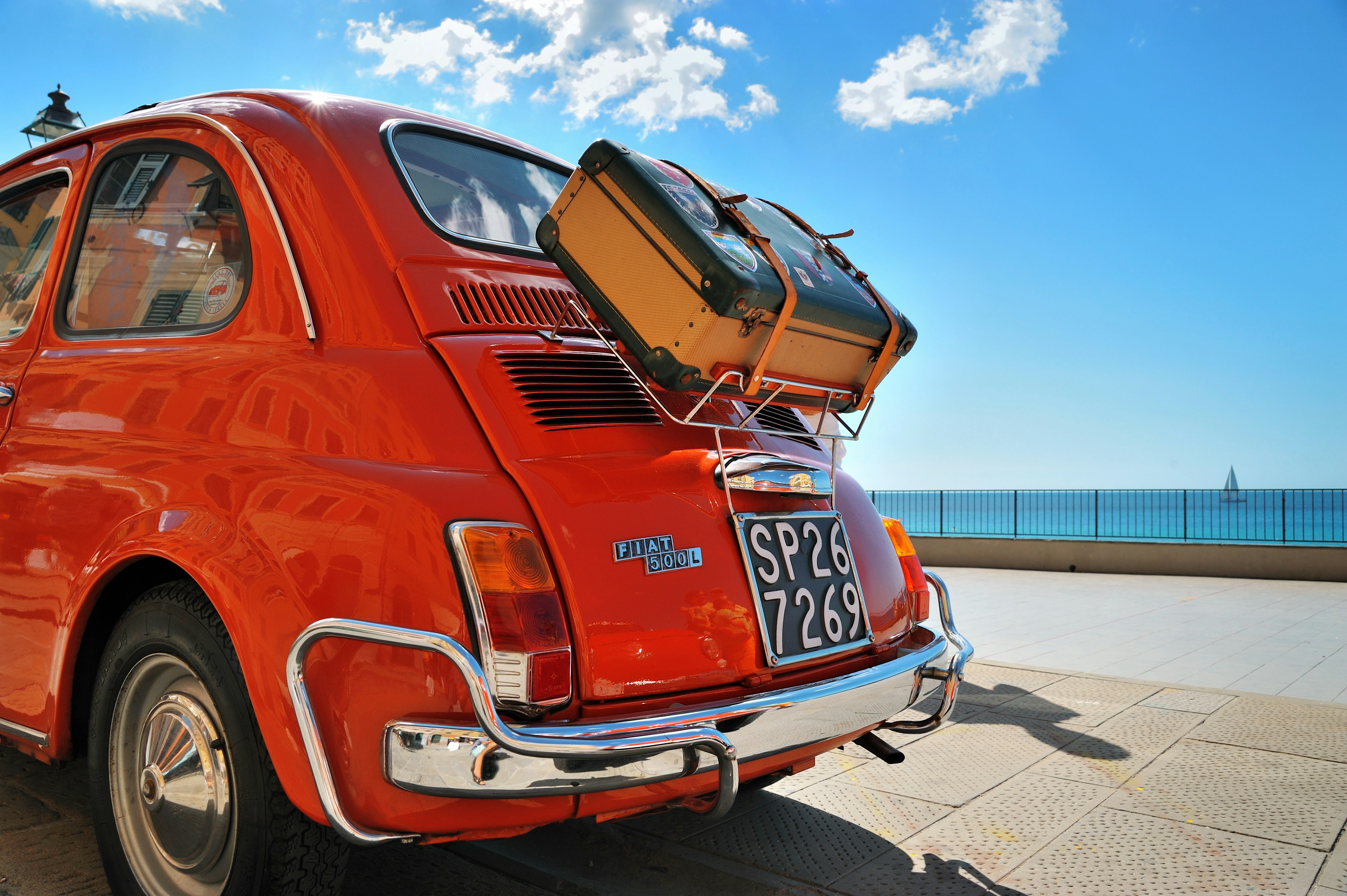 A small old style Fiat 500L car with a suitcase strapped to the back of it