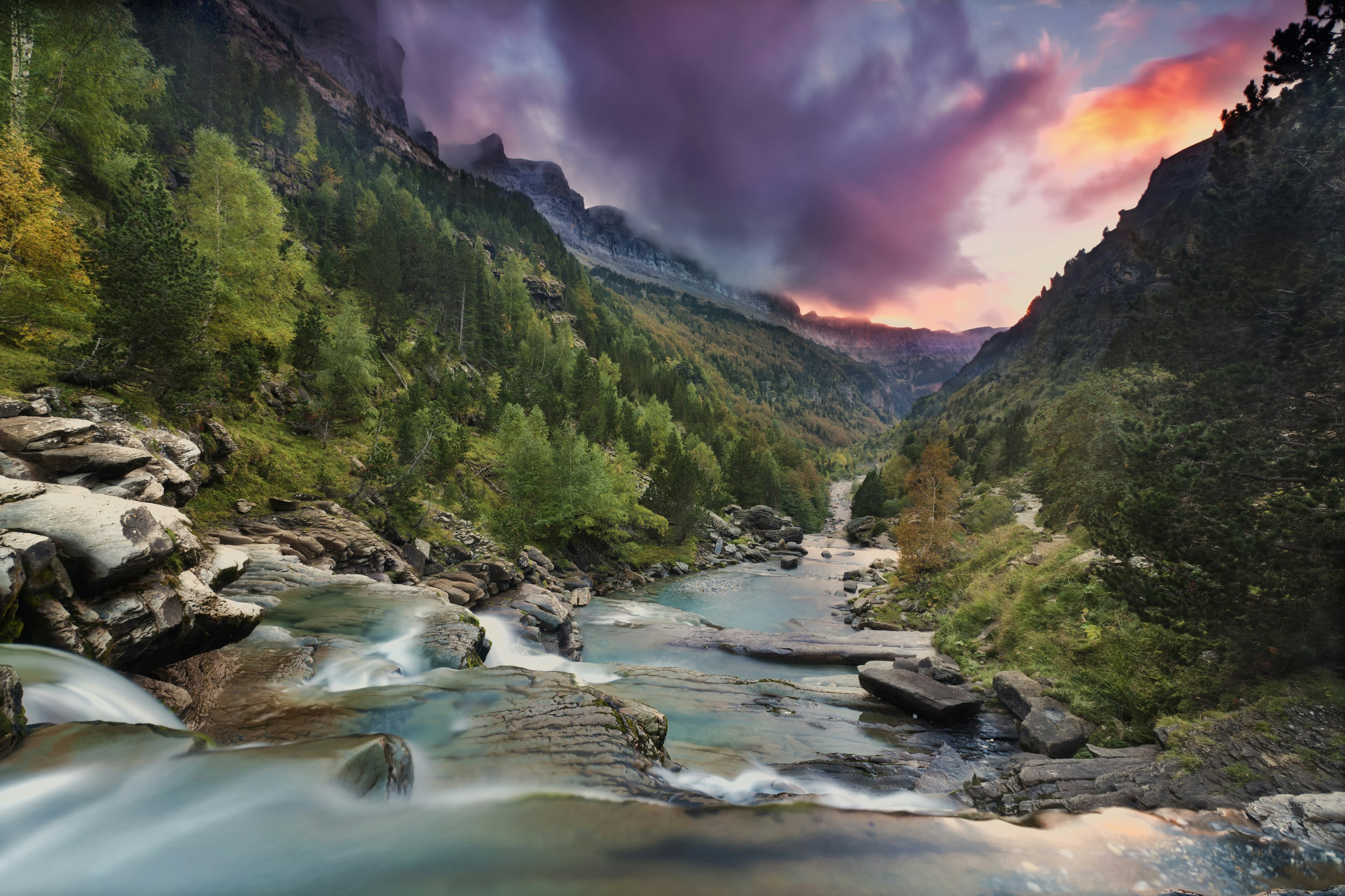 A river flows through the forested Ordesa Valley as the sun sets