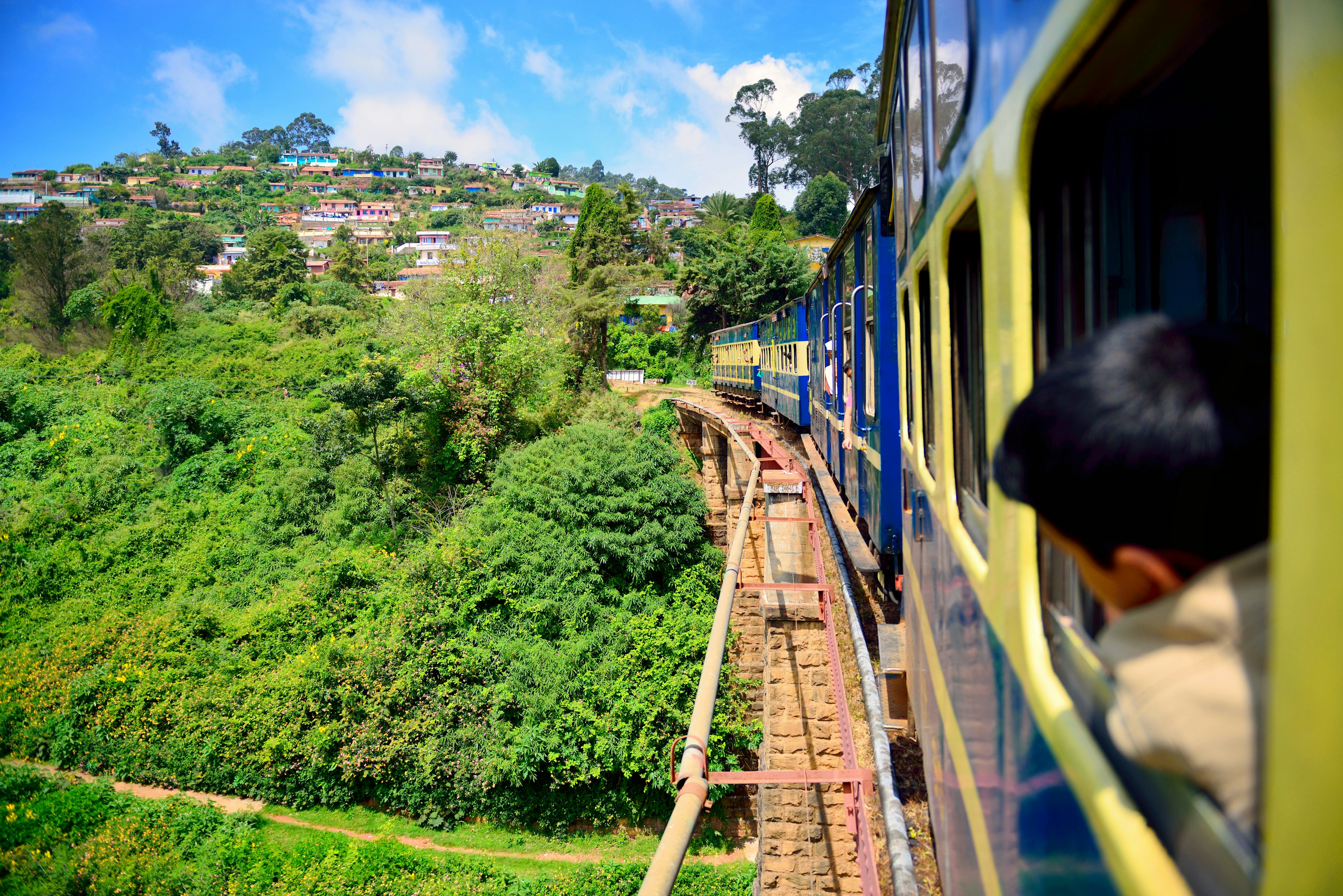 A train crossing a bridge curves through lush green hillsides in India