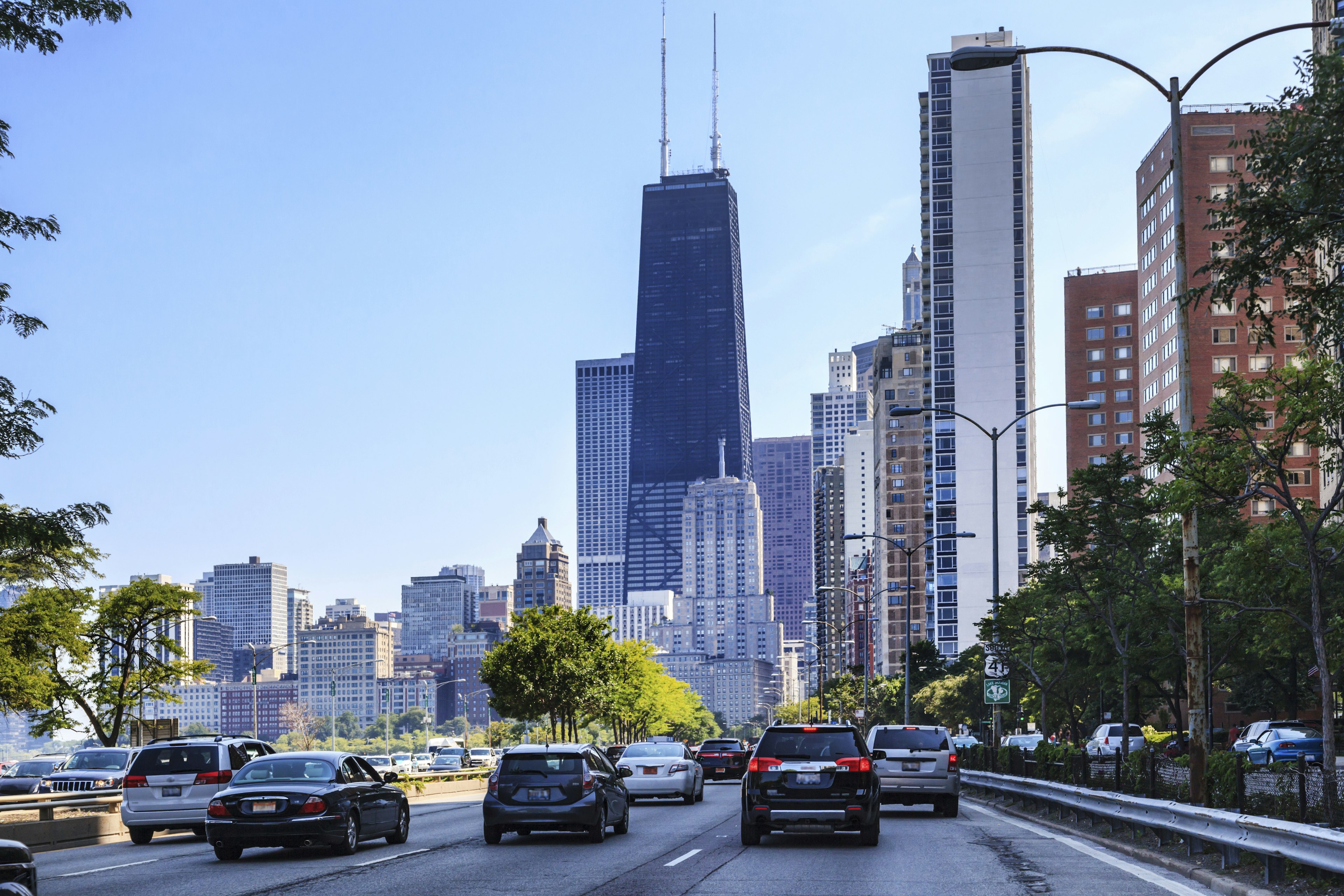 A street level view of traffic driving on Lake Shore in Downtown Chicago with skyscrapers in the background including the Sear's tower.