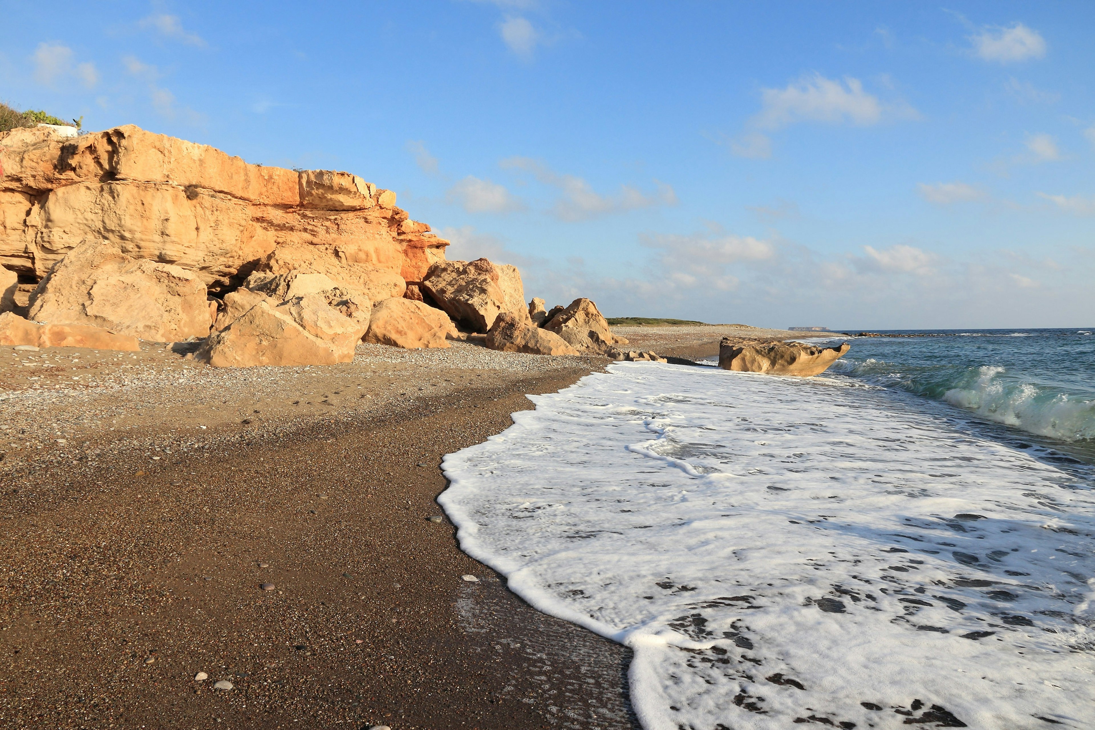 Waves lap at an empty beach backed by rocks