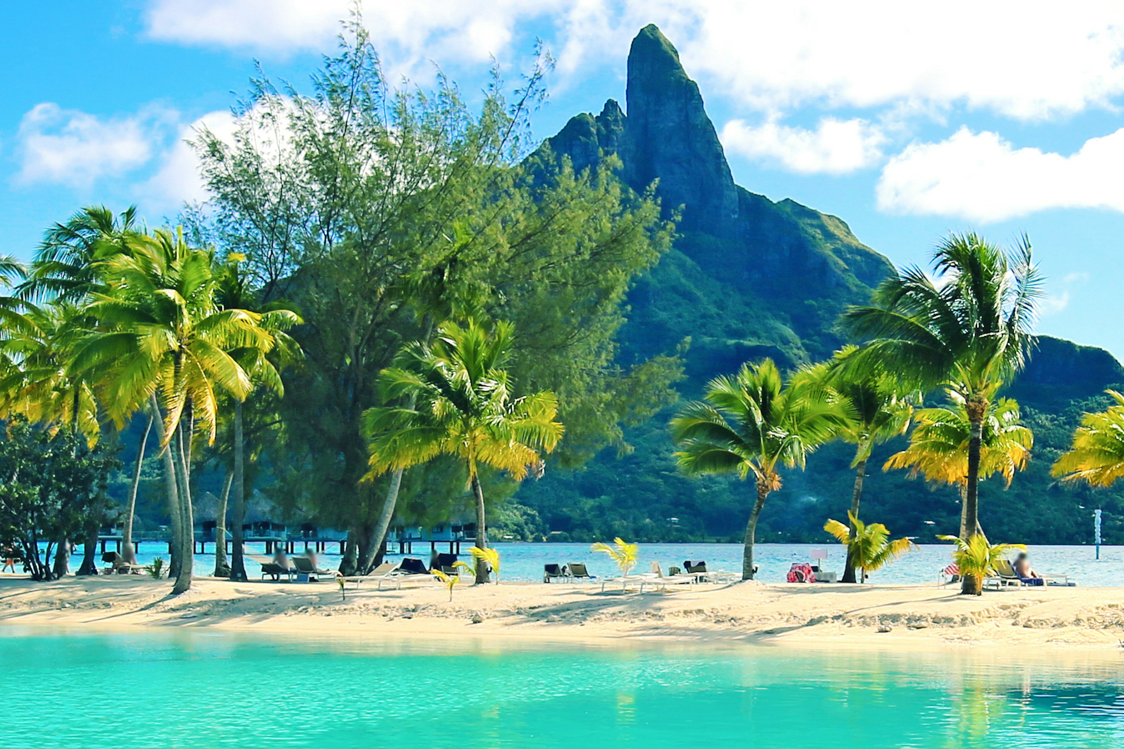 A strip of sand and palm trees in front of the lagoon and Mount Otemanu on Bora Bora.