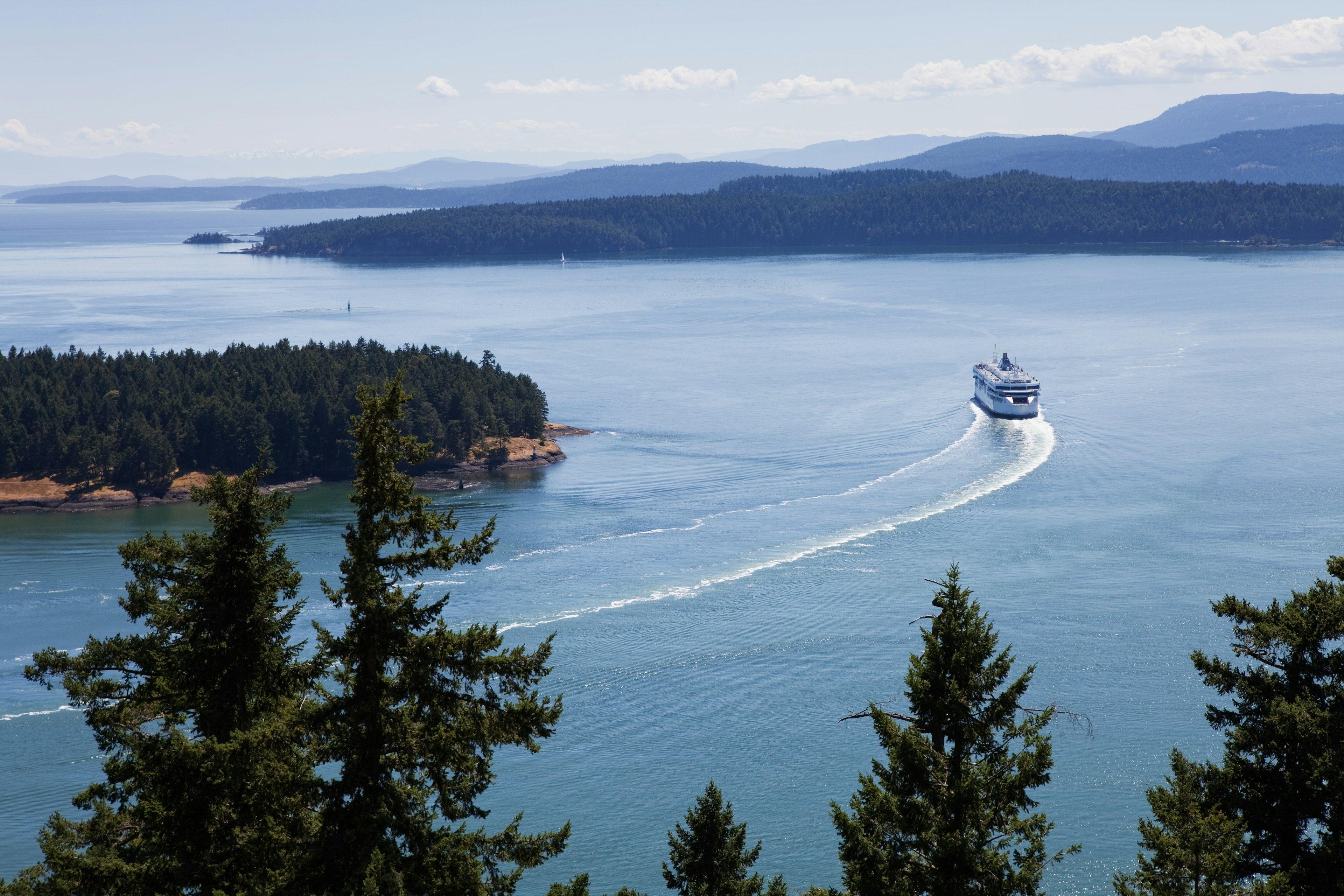 A ferry makes its way through a wide waterway between islands dense with trees