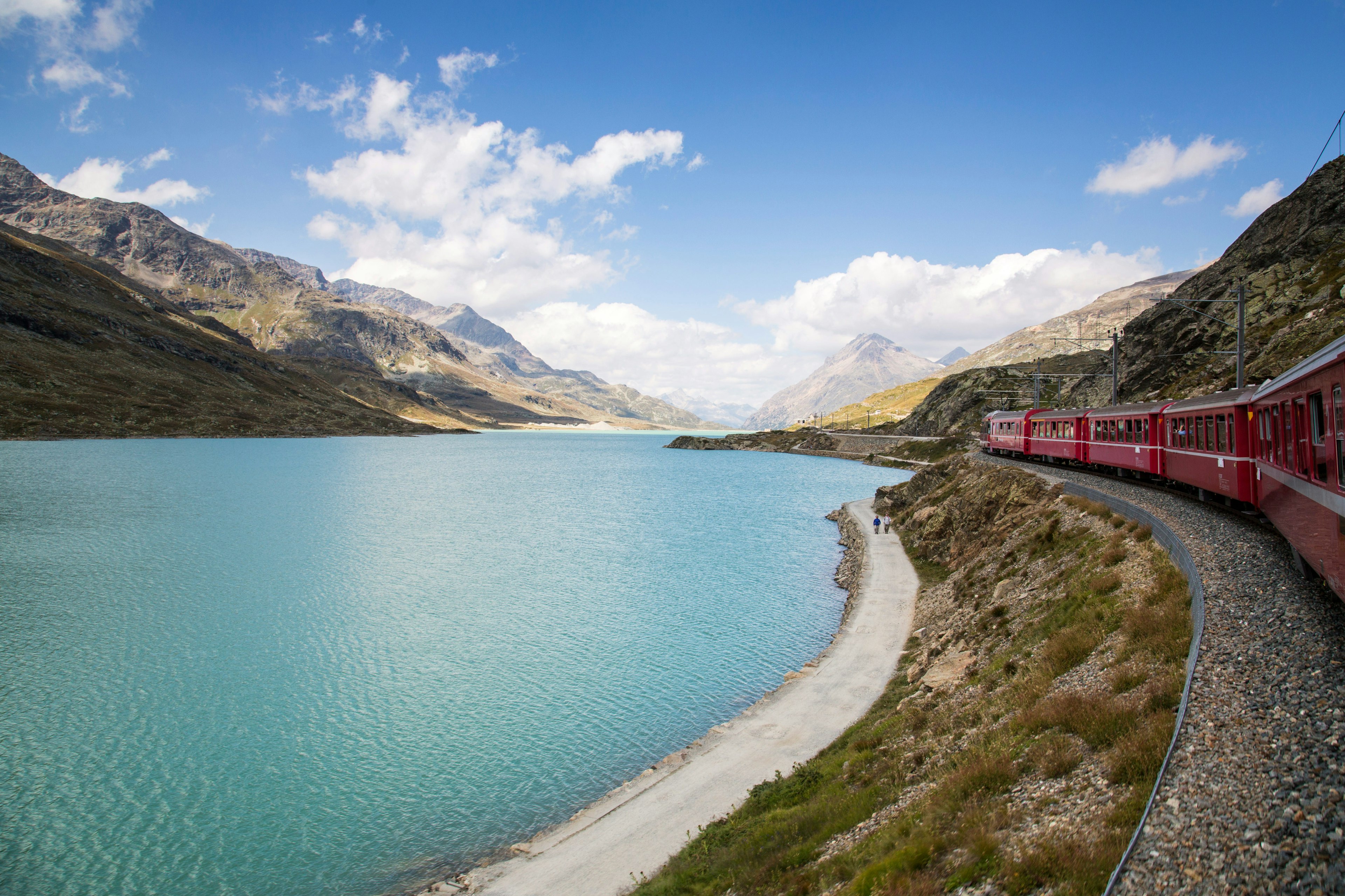 A red Bernina Express train travels along a lakeshore in Switzerland