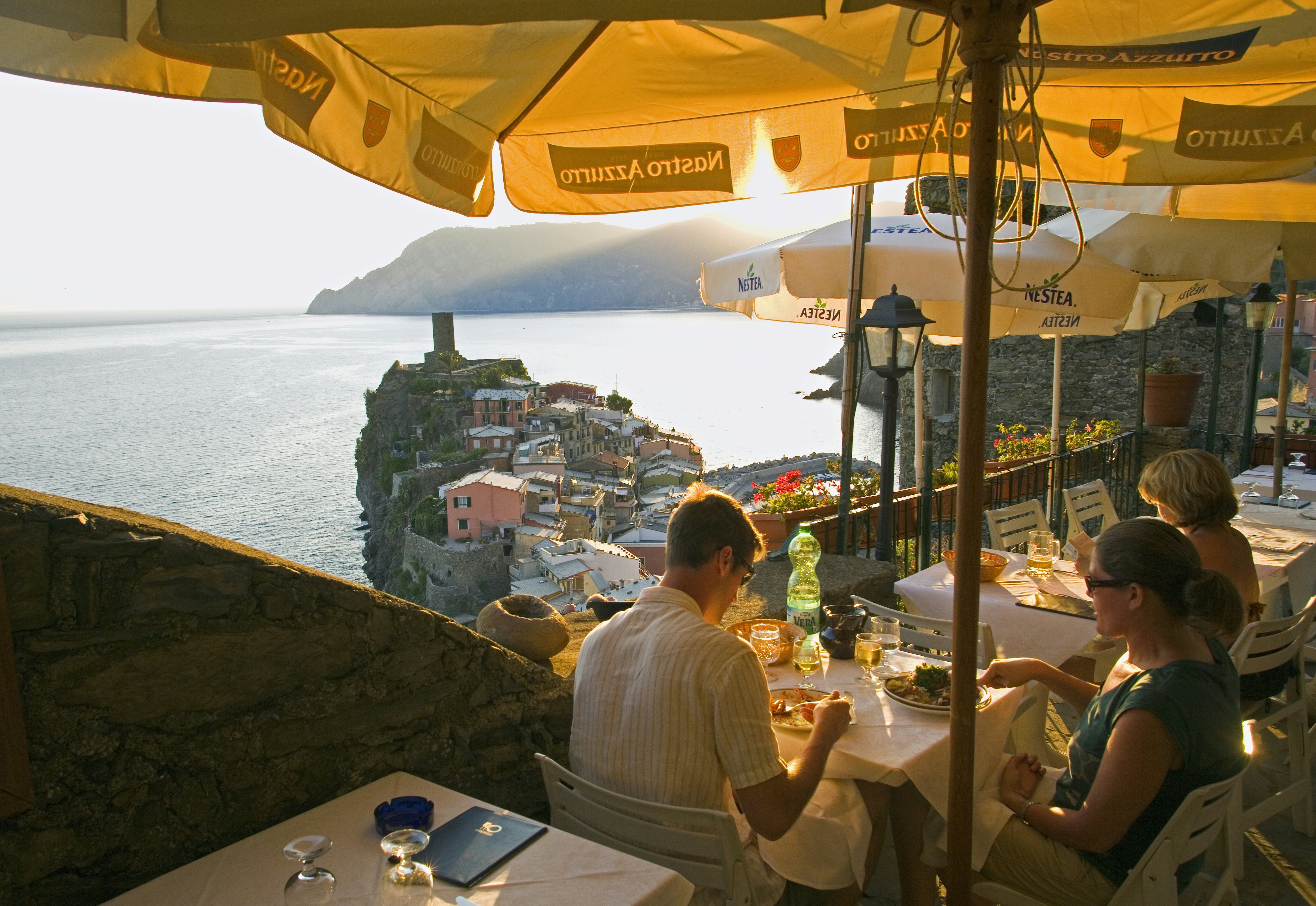 People eating on a clifftop restaurant terrace overlooking a small promontory and the ocean