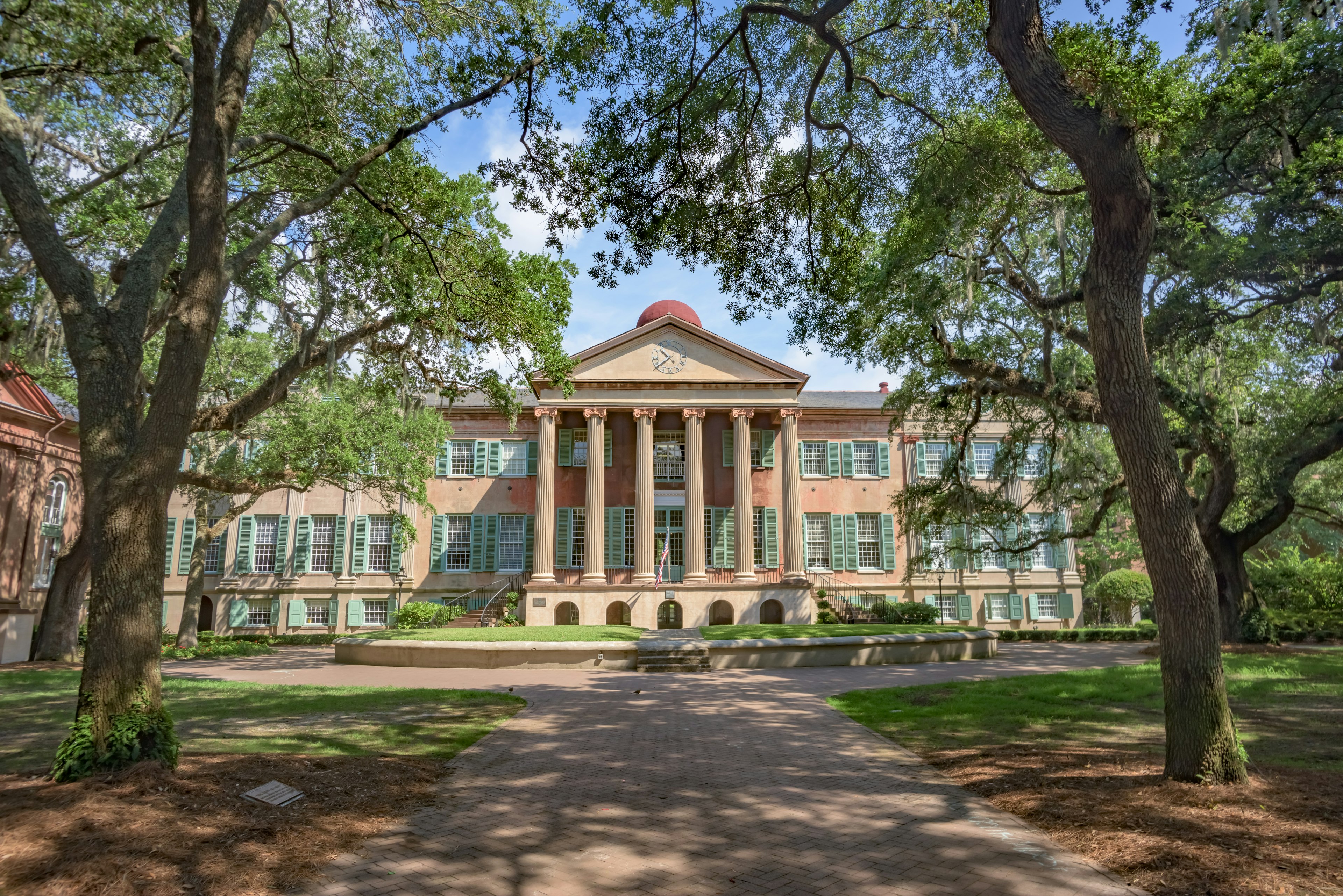 Randolph Hall, the main academic building on the College of Charleston campus, sits behind the shade of trees on the lawn.