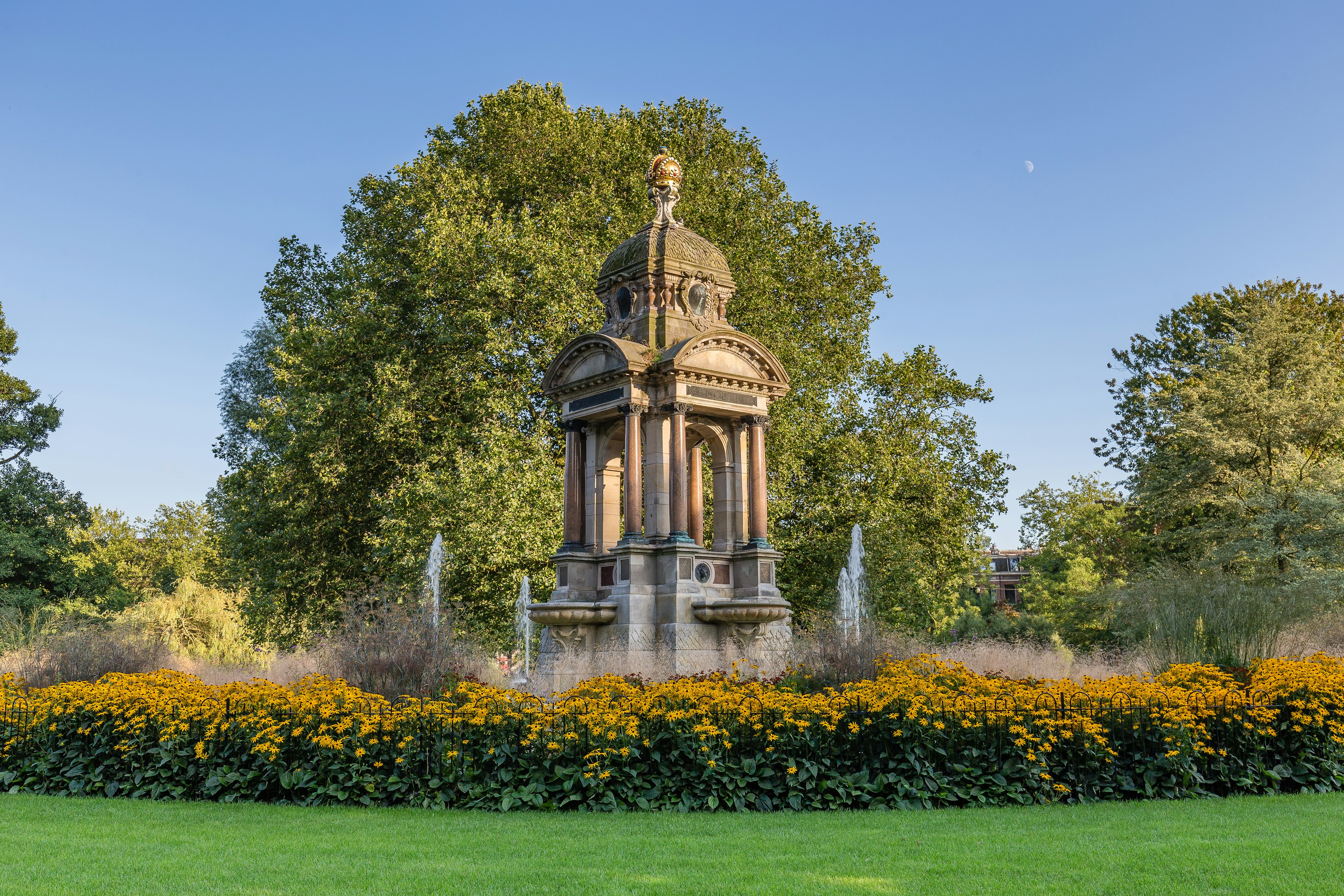 A free-standing stone monument in the center of a fountain surrounded by flowers