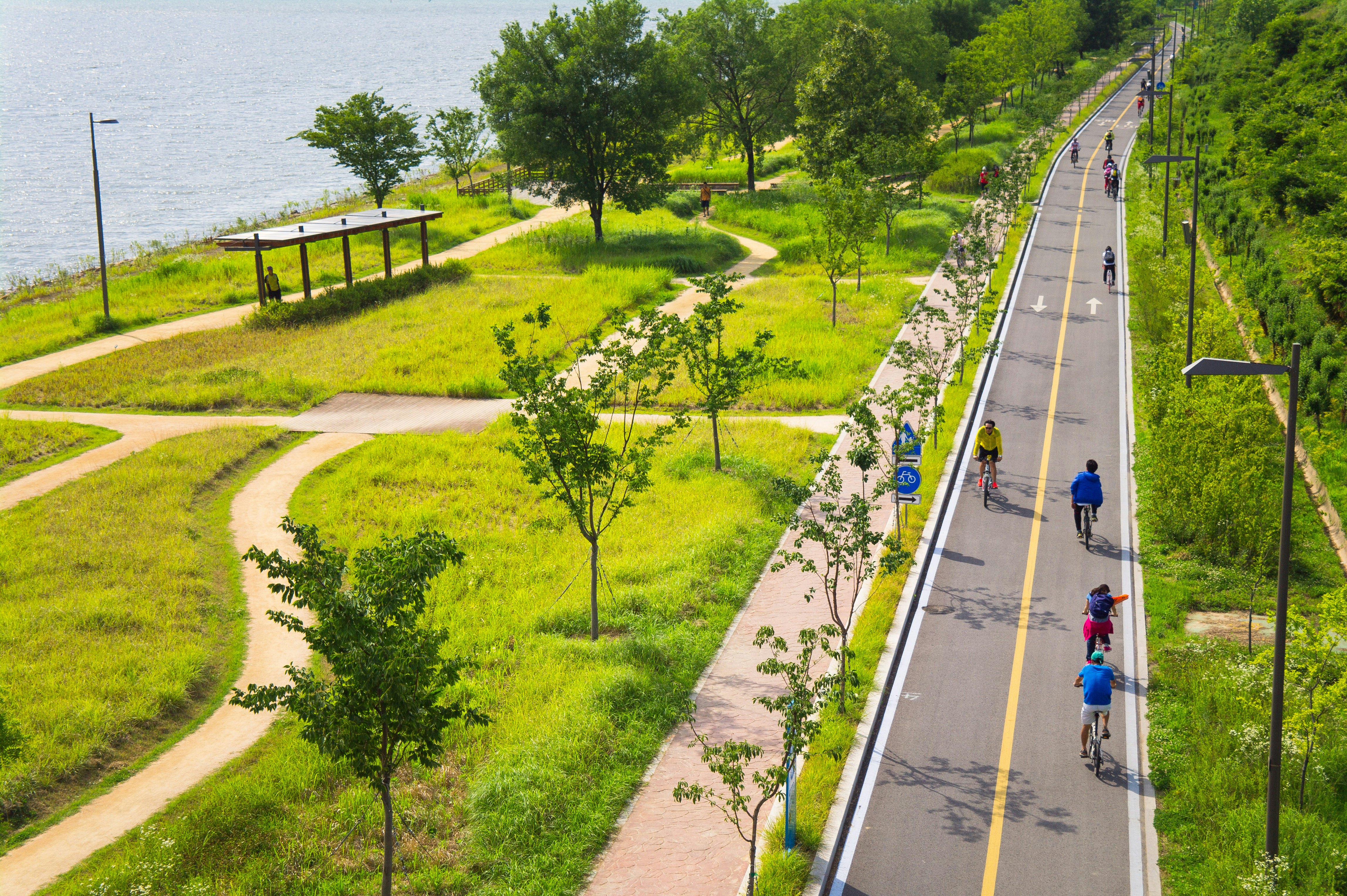 Cyclists ride along a paved bicycle path beside a river.