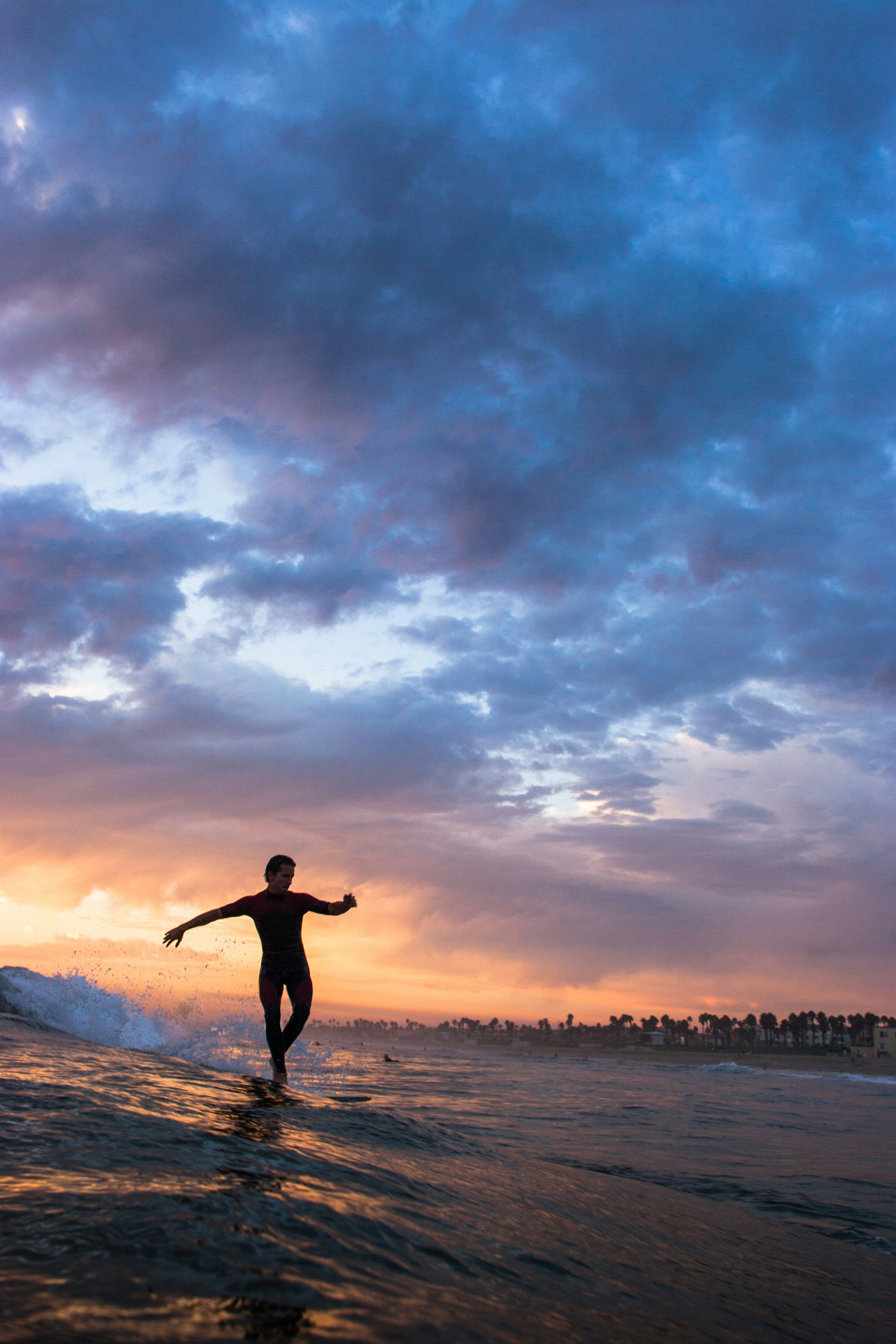 Silhouette of a surfer walking to the nose of his longboard at sunset