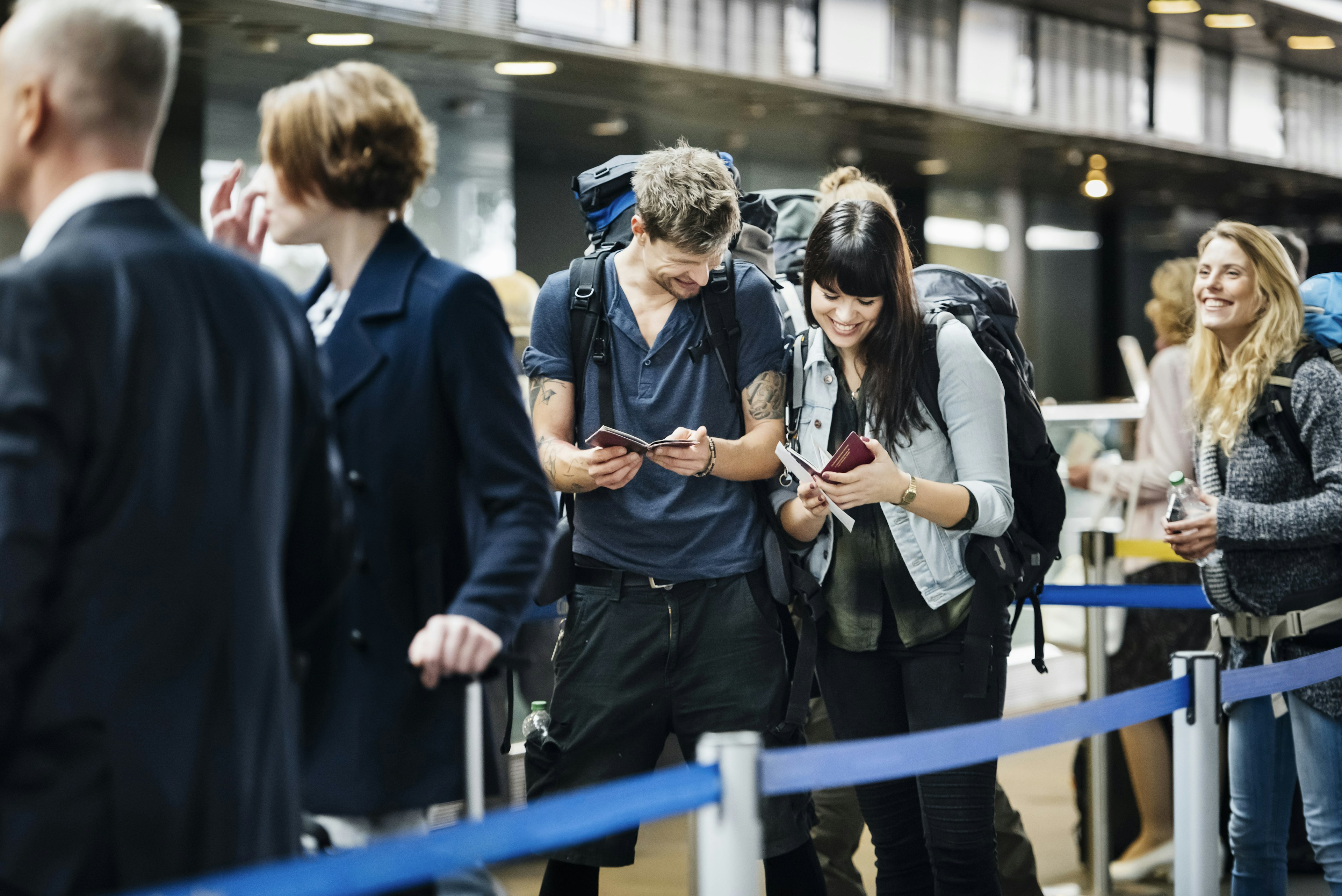 Young backpacker couple smiles as they wait with other people at the check-in counter at an airport