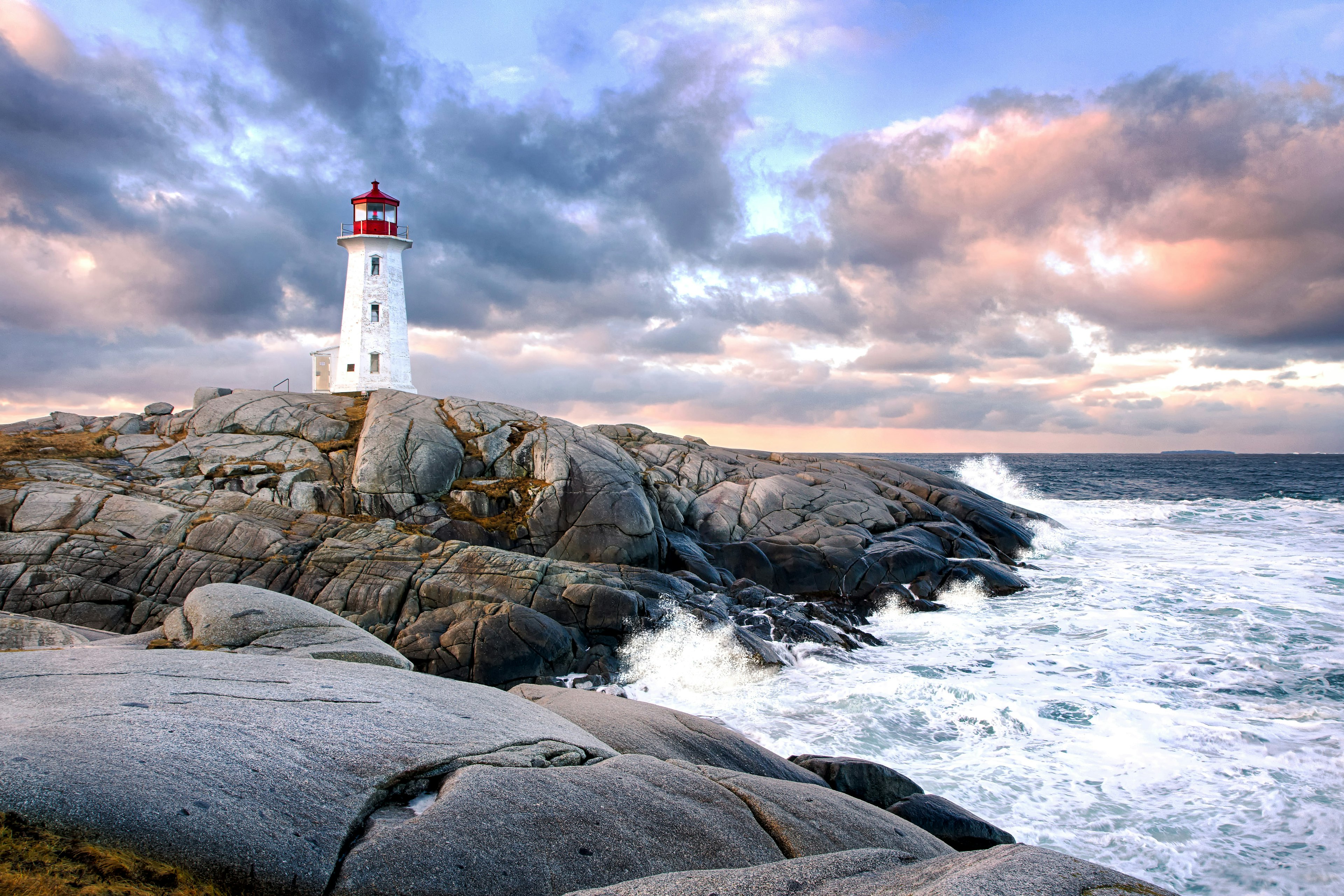 Peggy's Cove Lighthouse during sunset with waves crashing against the rocks.