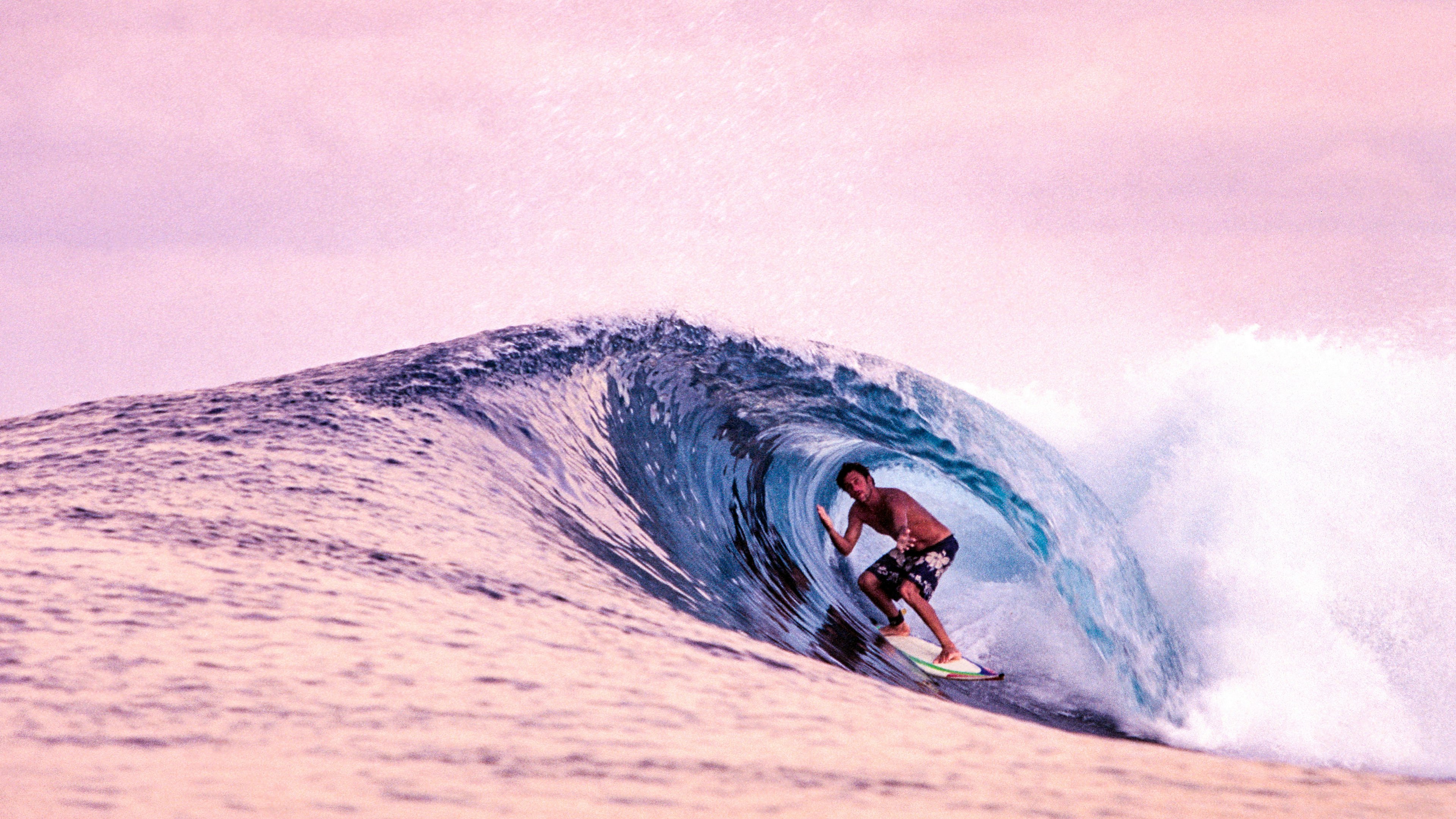 A surfer in a barrel in the Indian Ocean against a pink-hued sky