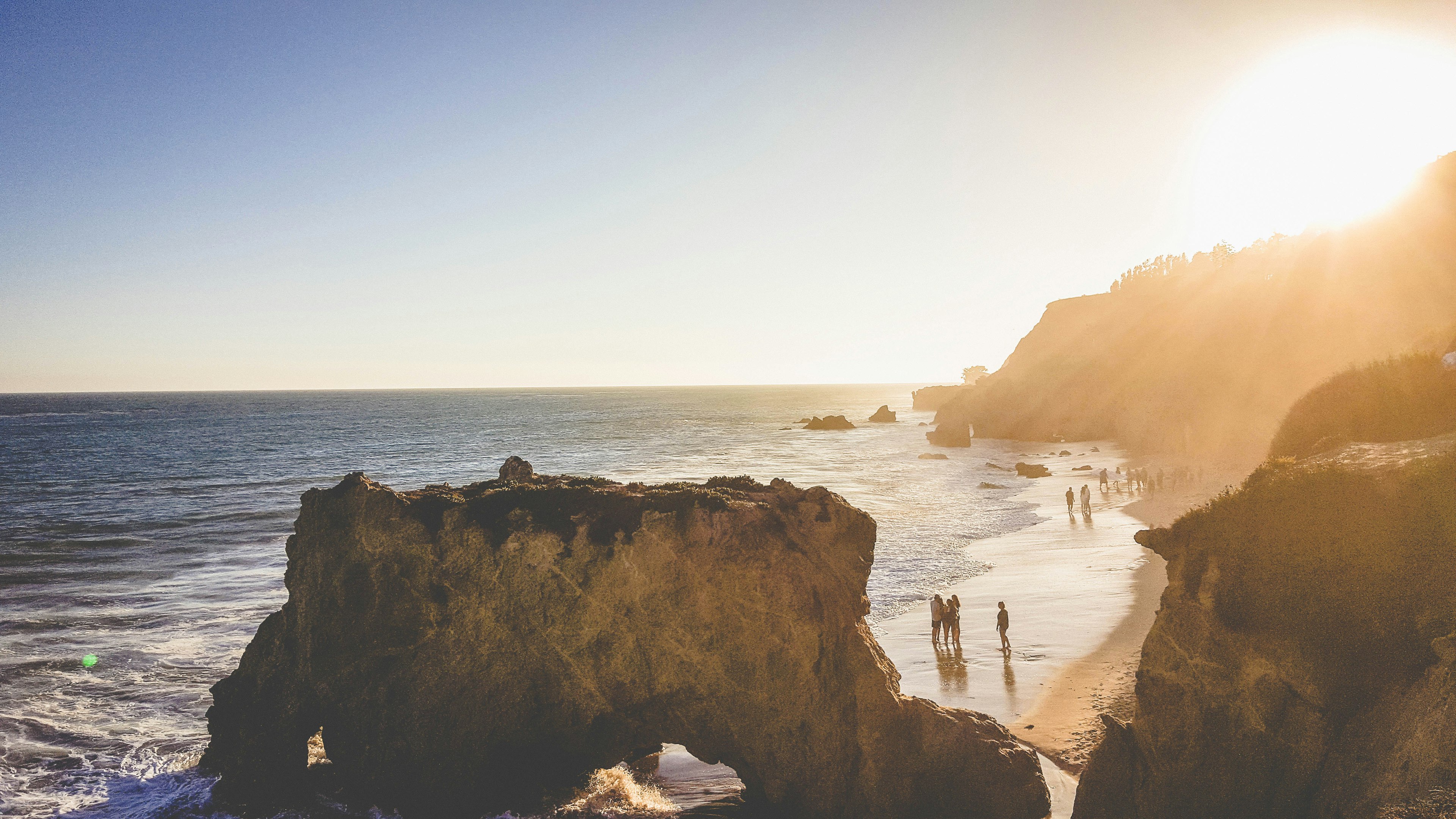 People walk along the sandy beach between rock formations on a sunny day