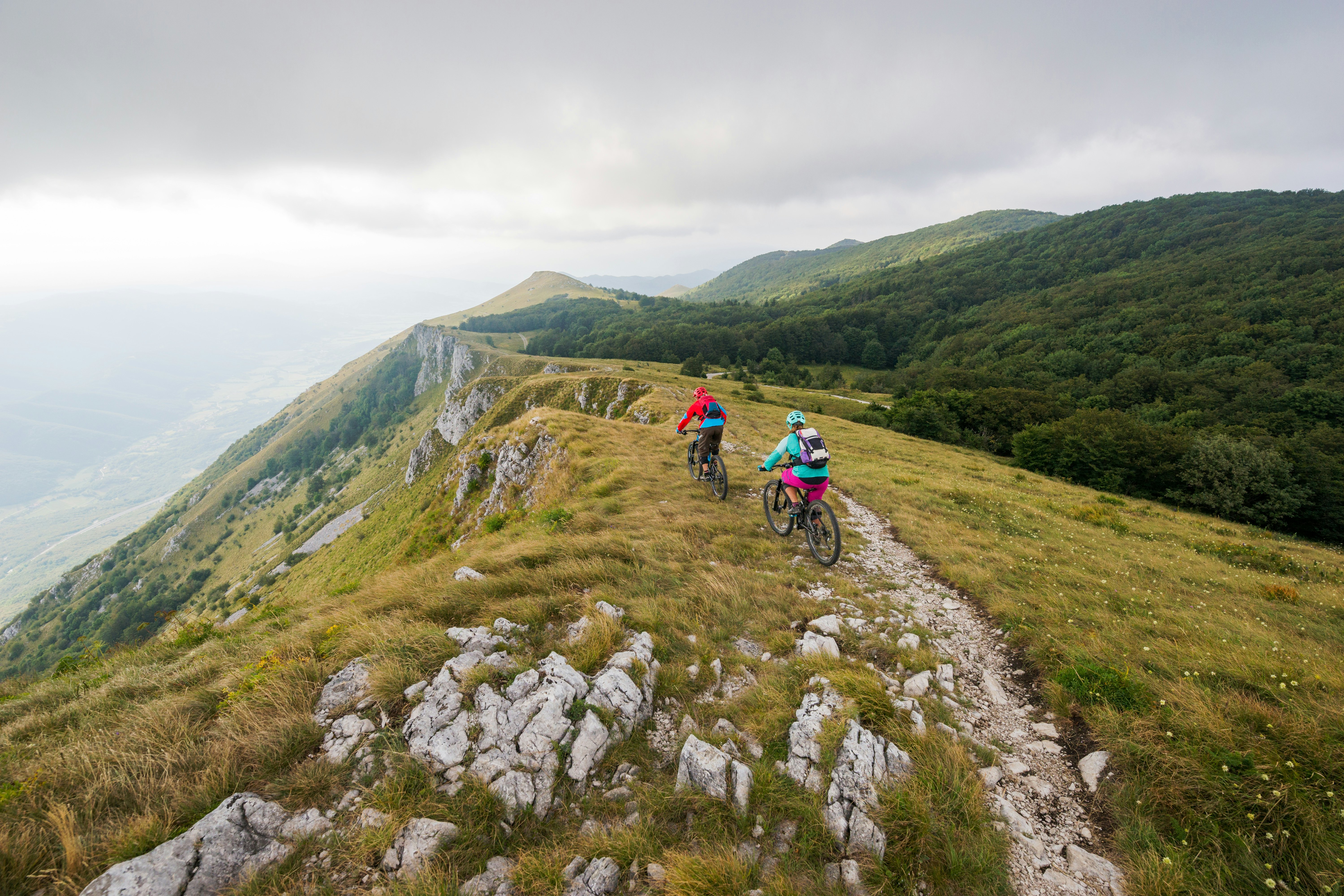 Two people mountain biking on a clifftop trail