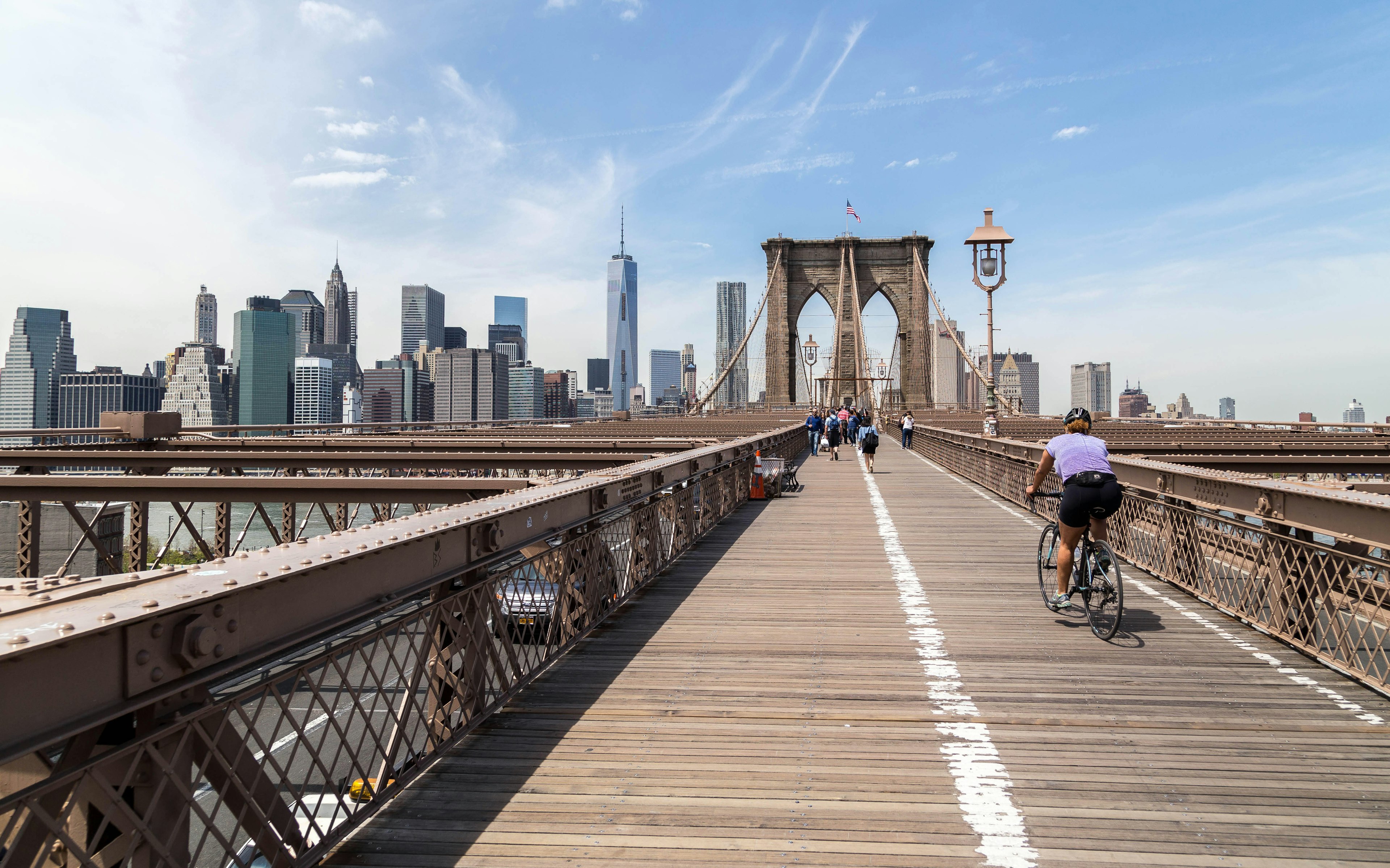 Rear View Of Woman Cycling On Brooklyn Bridge In City Against Sky