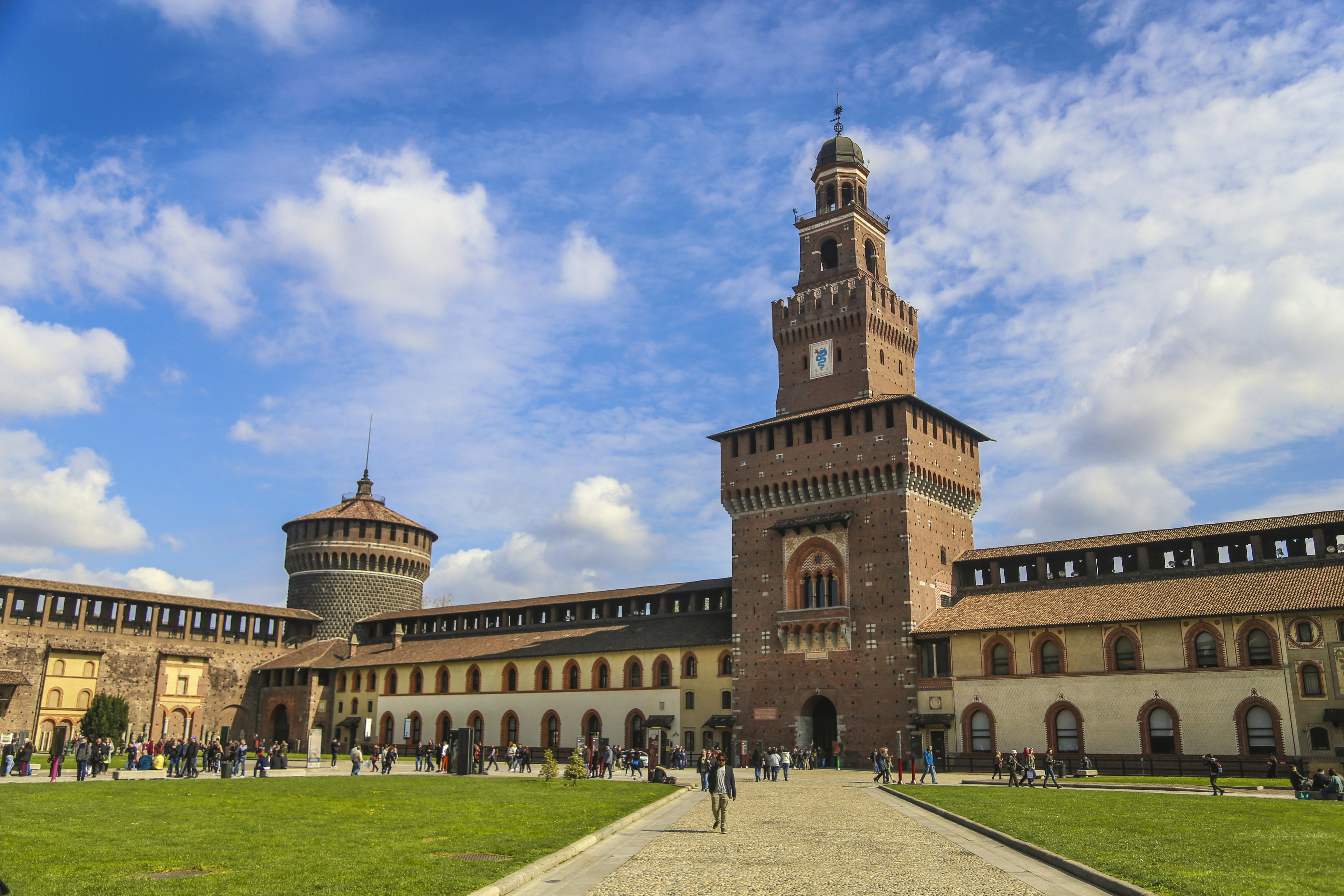 The grounds of a large castle courtyard with tourists strolling the paths.