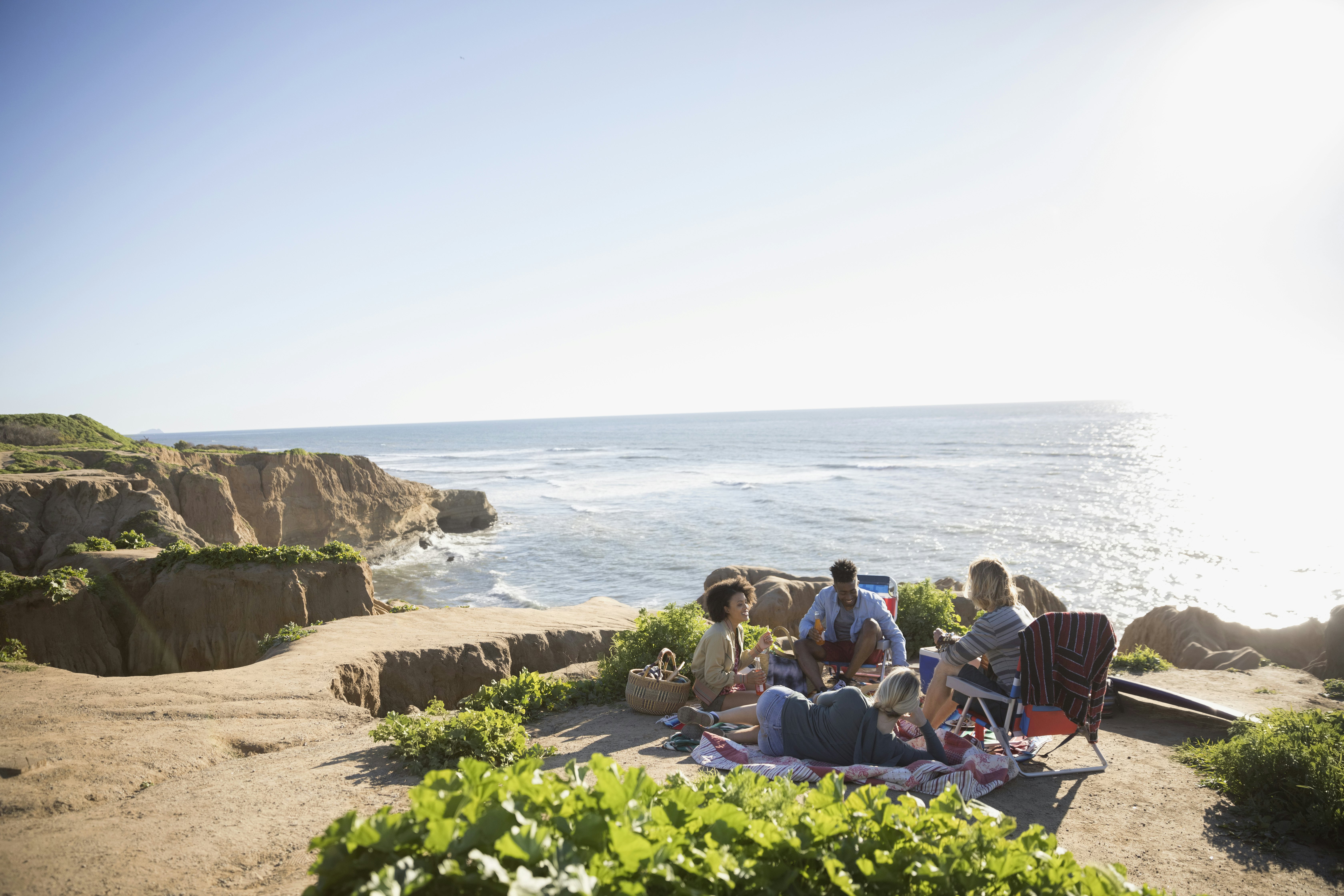 Young friends hanging out on a sunny clifftop with the ocean beyond.