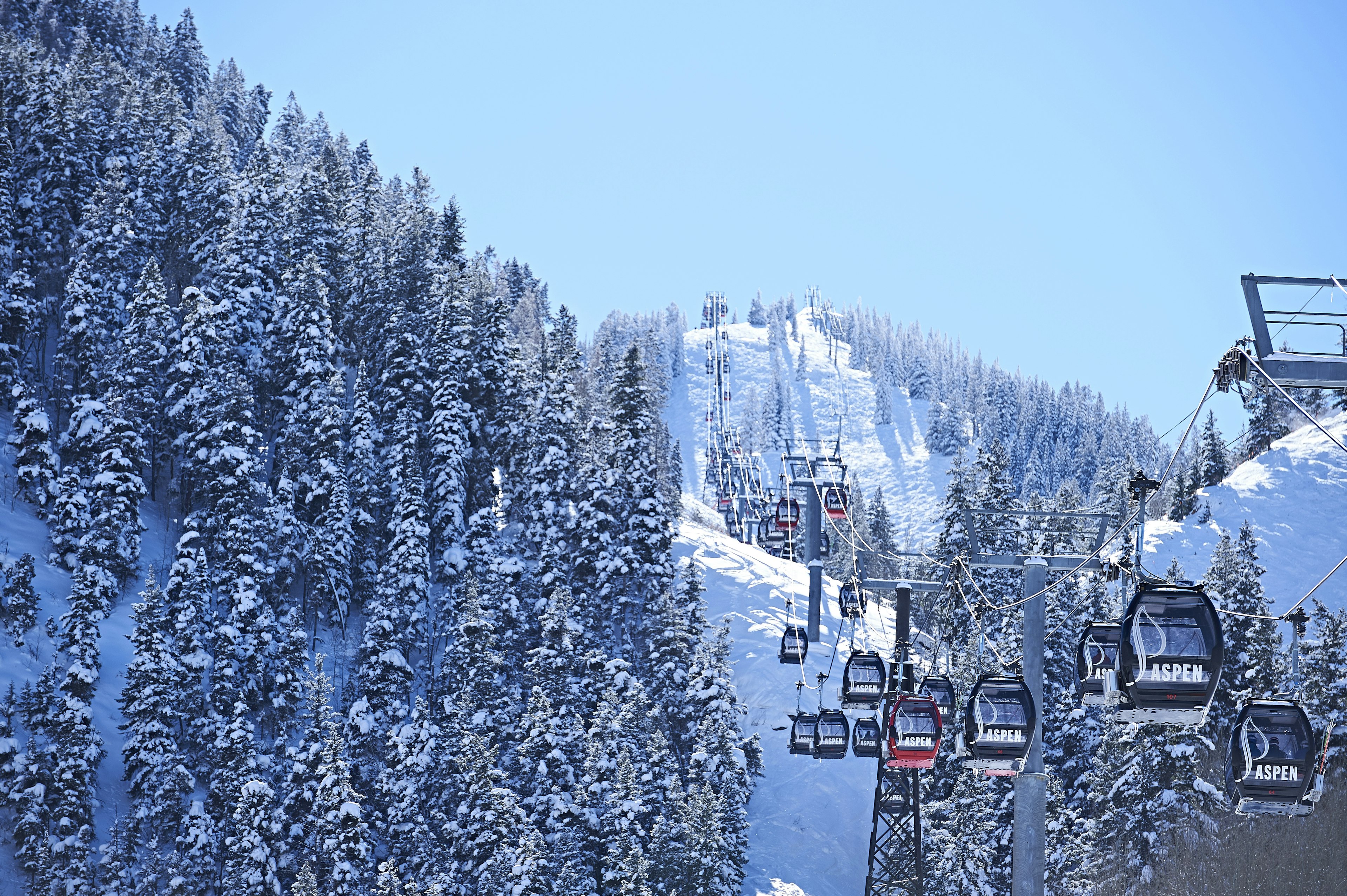 Cable car moving up over forested snow covered mountains, Aspen, Colorado, USA