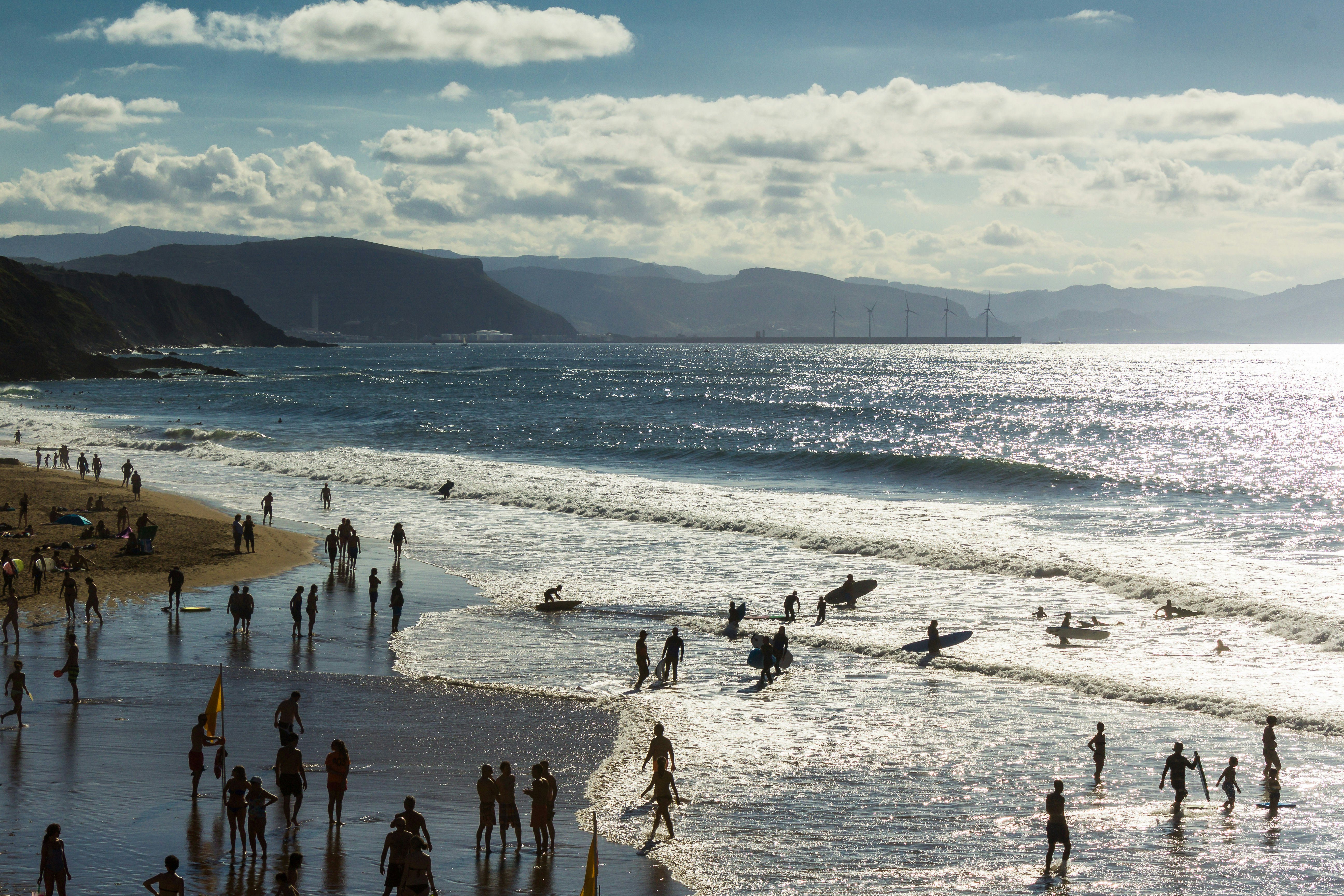 Beach-goers in silhouette on a beach. Many surfers are heading out to the ocean, where large waves are building