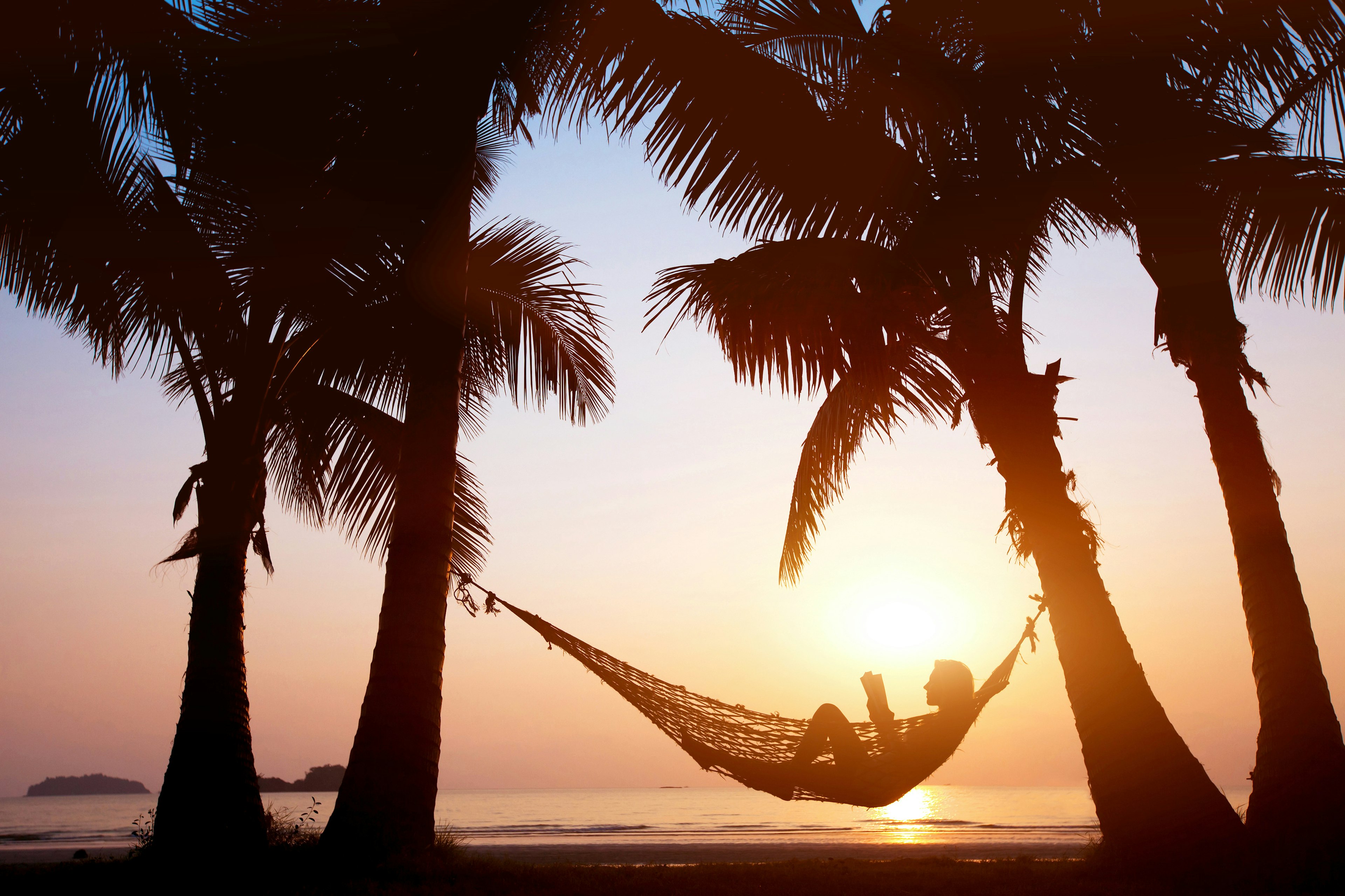 Silhouette of a woman relaxing in a hammock on a beach during sunset. 