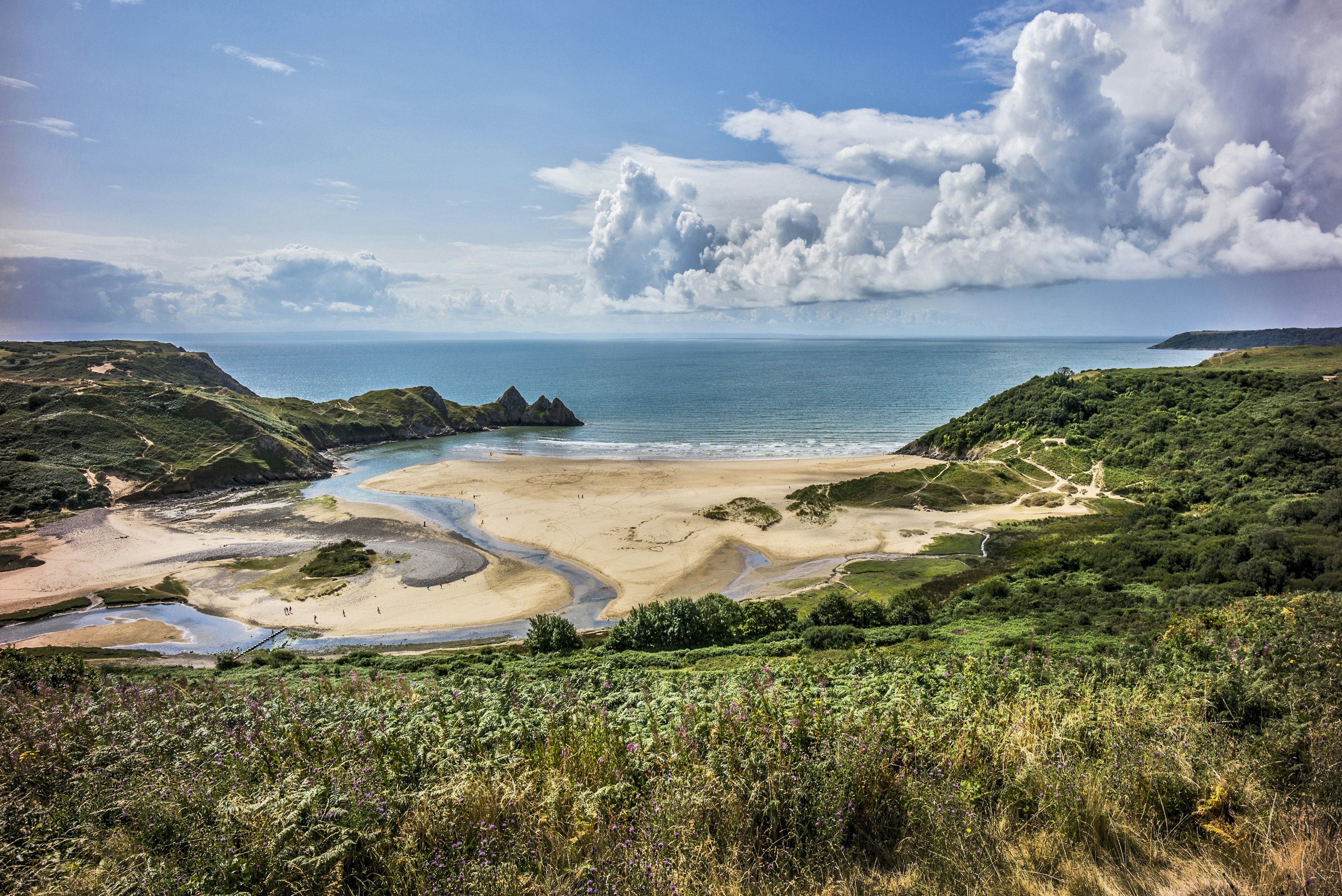 A curved golden beach, with three distinct peaks where the land dips into the sea