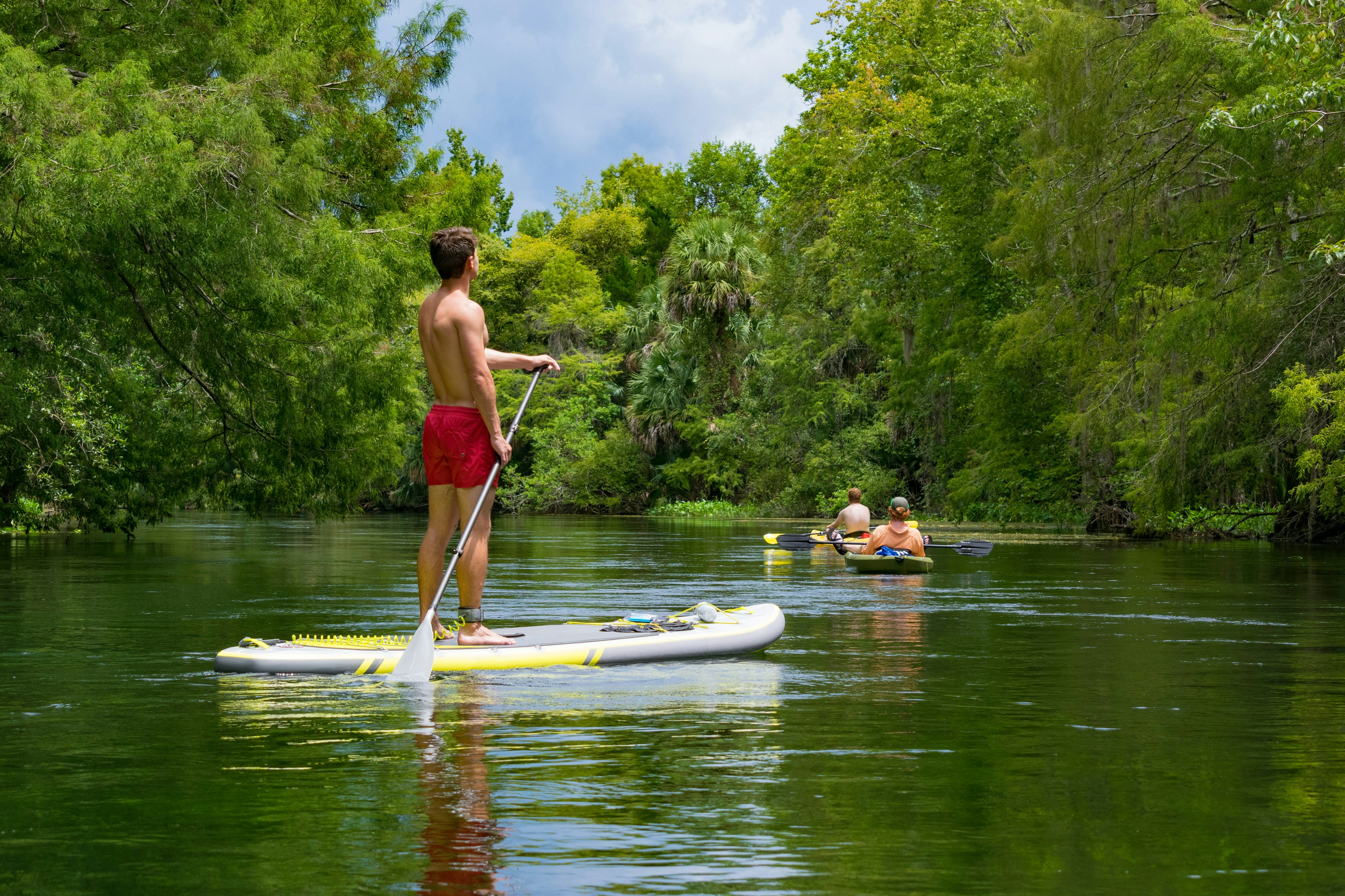 A male standup paddleboarder and two kayakers go down a river