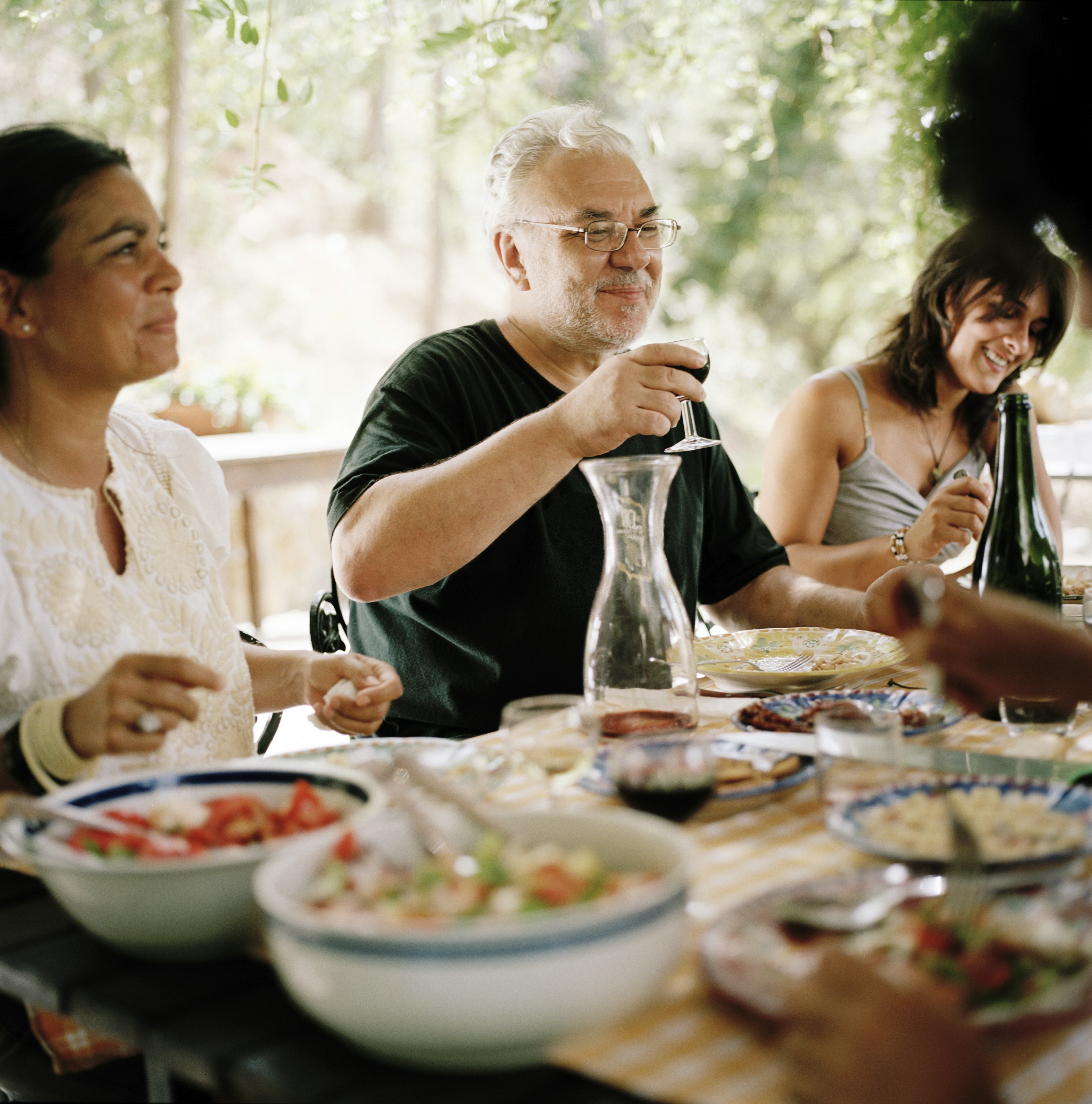 Two women and a man eat together at a table sharing food and wine