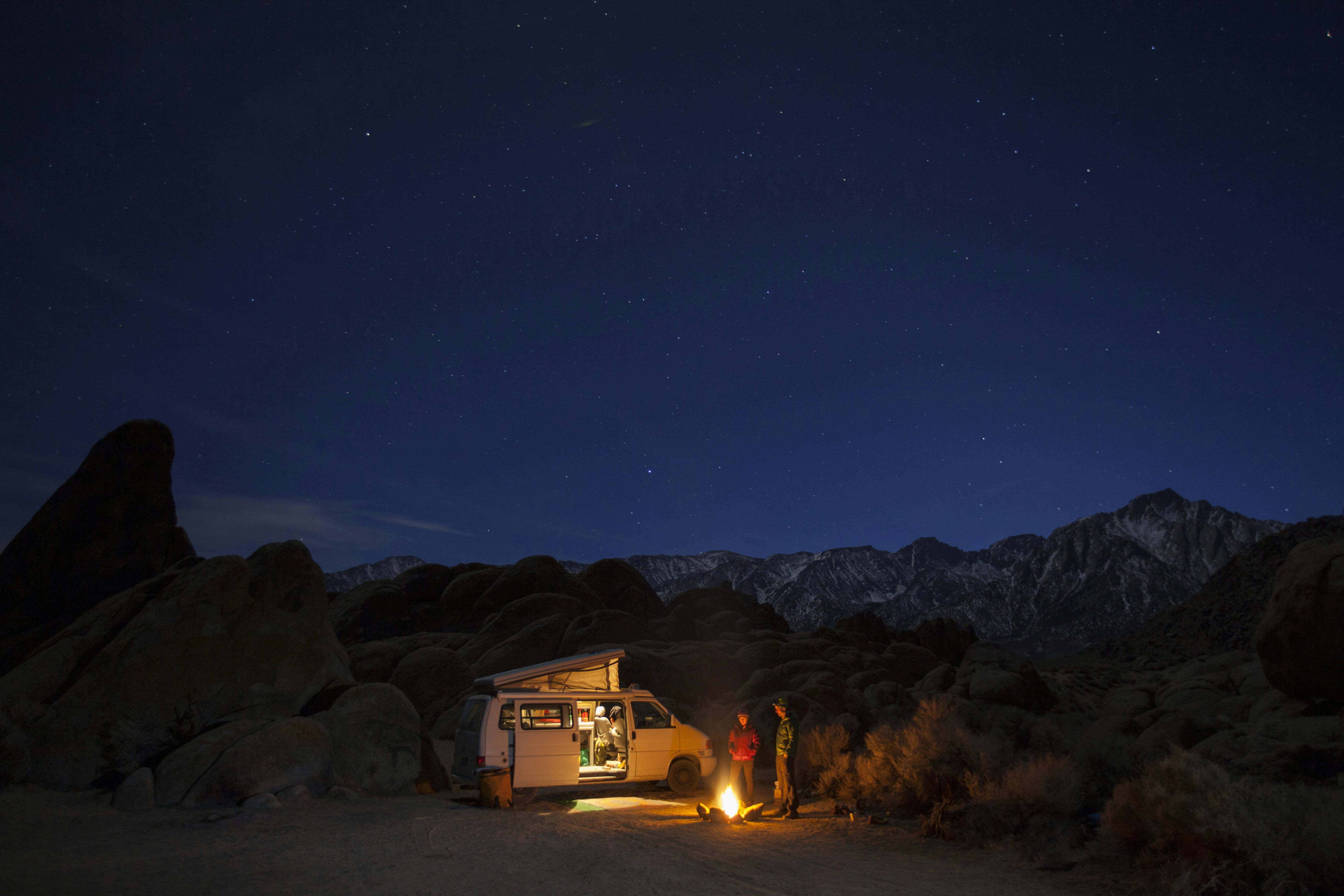 Two friends standing by campfire at night while camping in Alabama Hills Recreation Area, Lone Pine, California, USA.