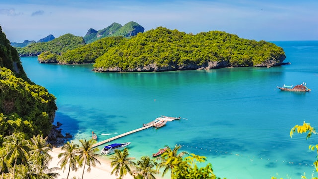 A boat floats by a small island covered in green undergrowth