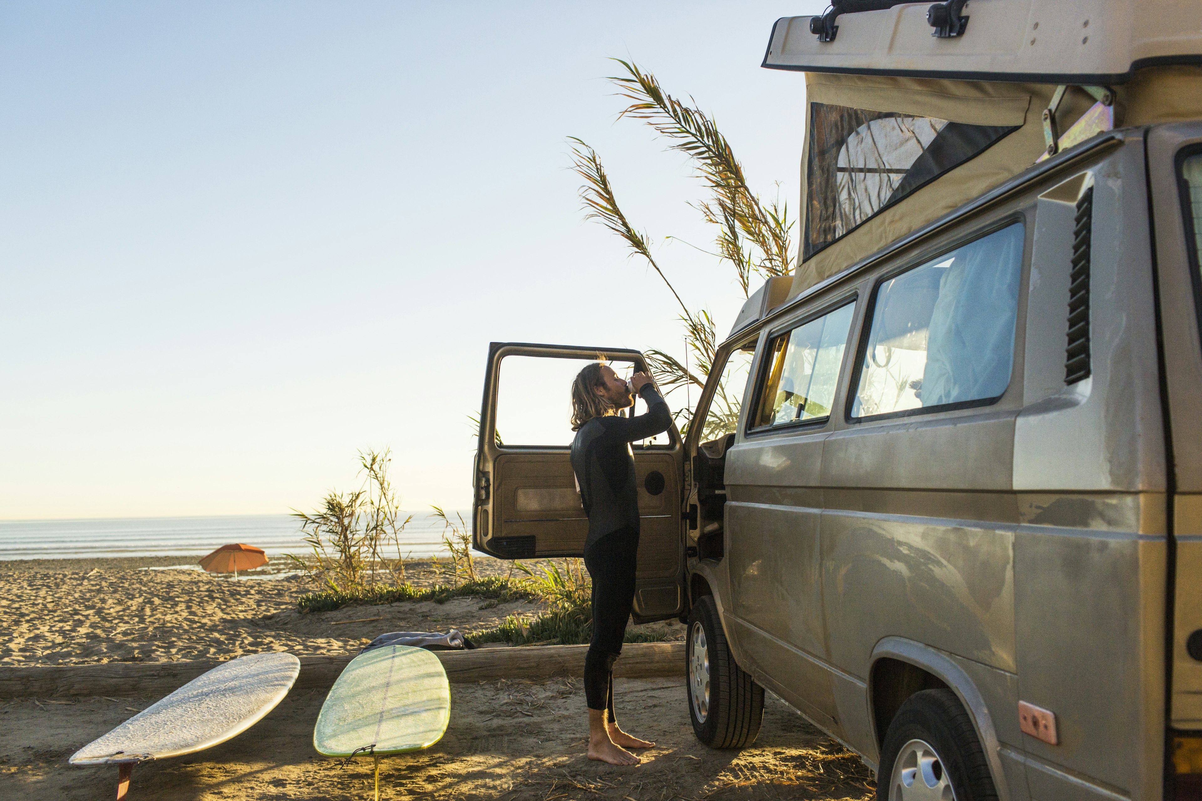 Side view of male surfer having drink outside mini van on San Onofre State Beach