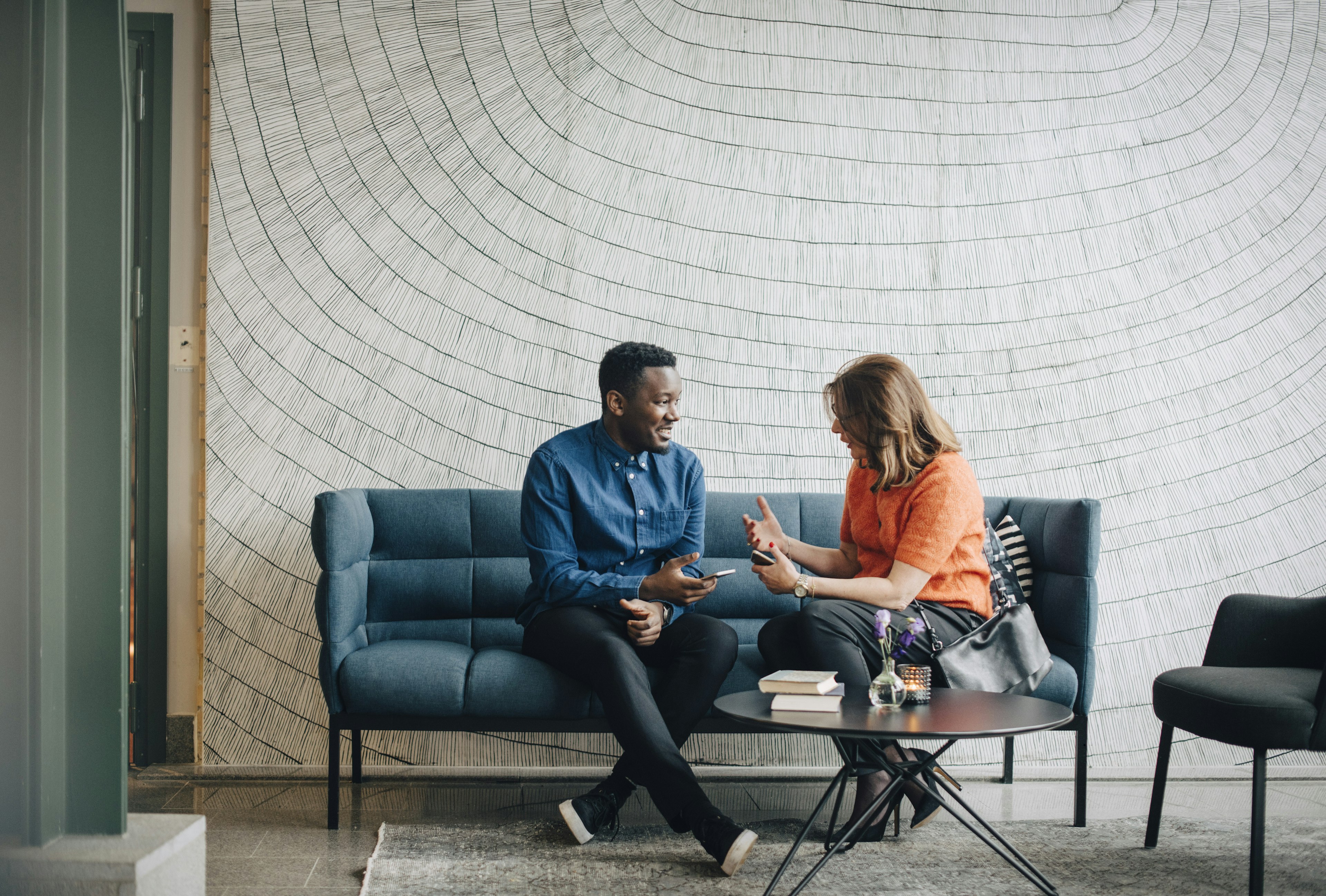 Businessman and woman taking while sitting on couch against wall at conference