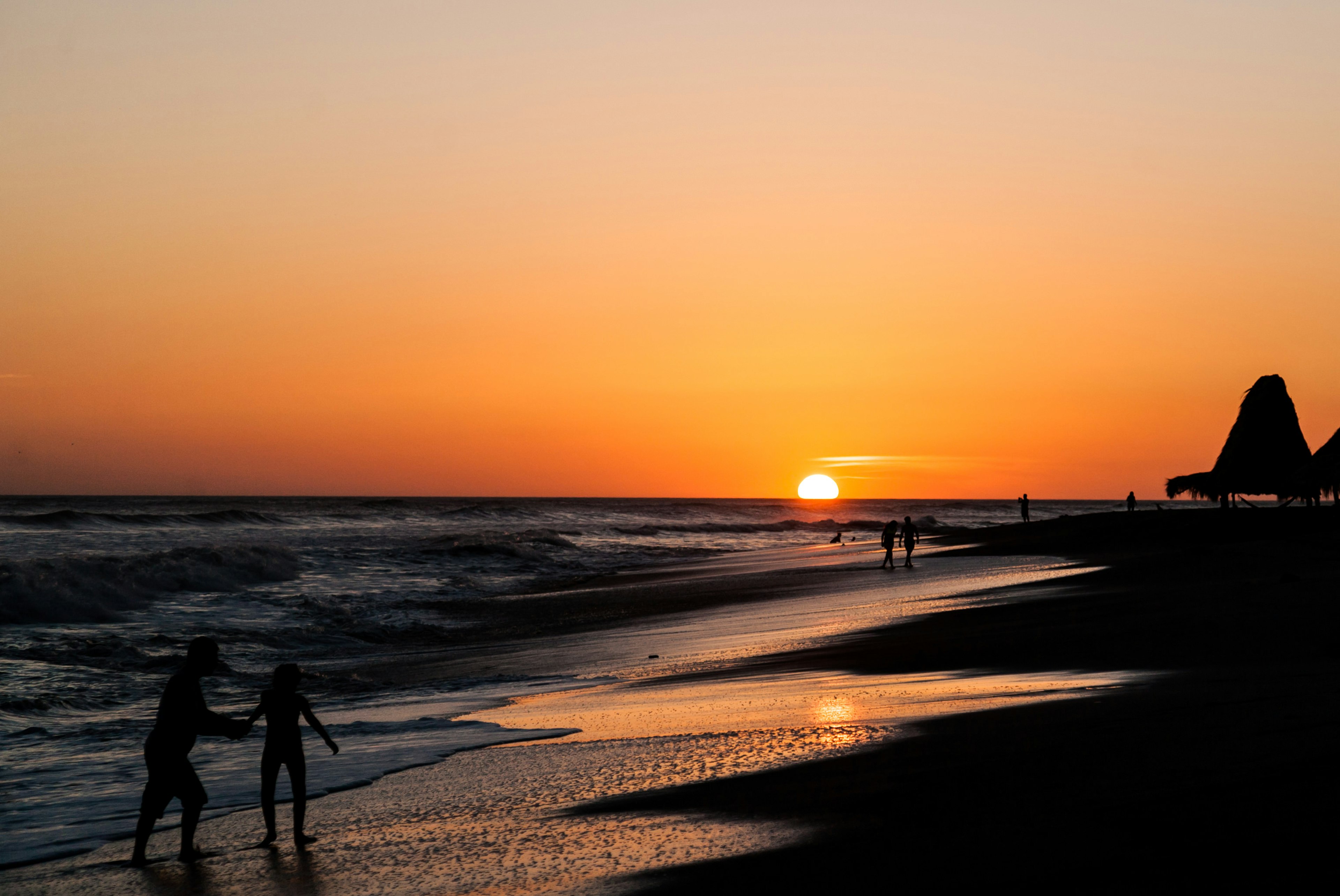 Two people old hands while walking in the surf as the sun sets on the horizon