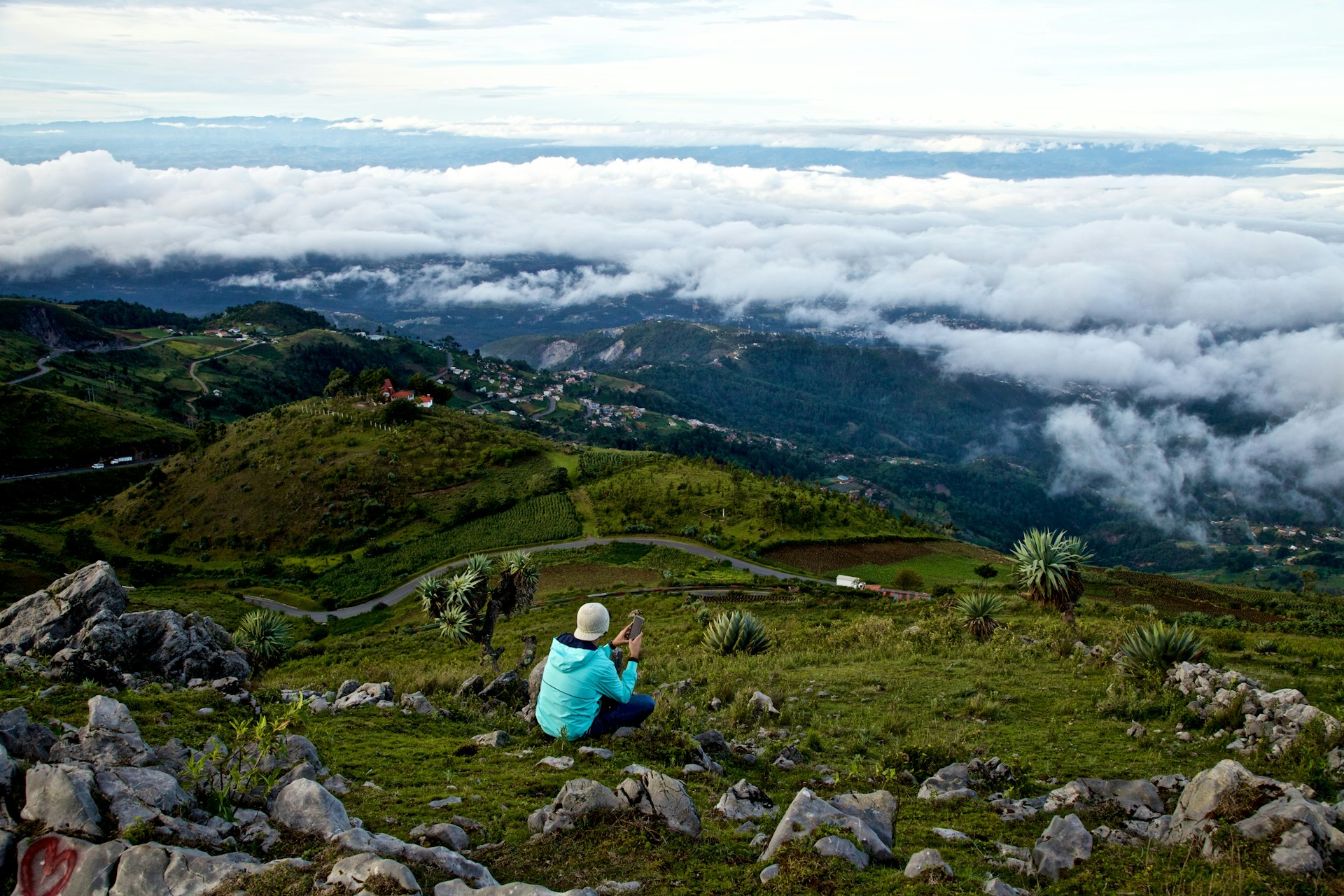 A man looks out over rolling green hills and low clouds in the Guatemalan highlands.