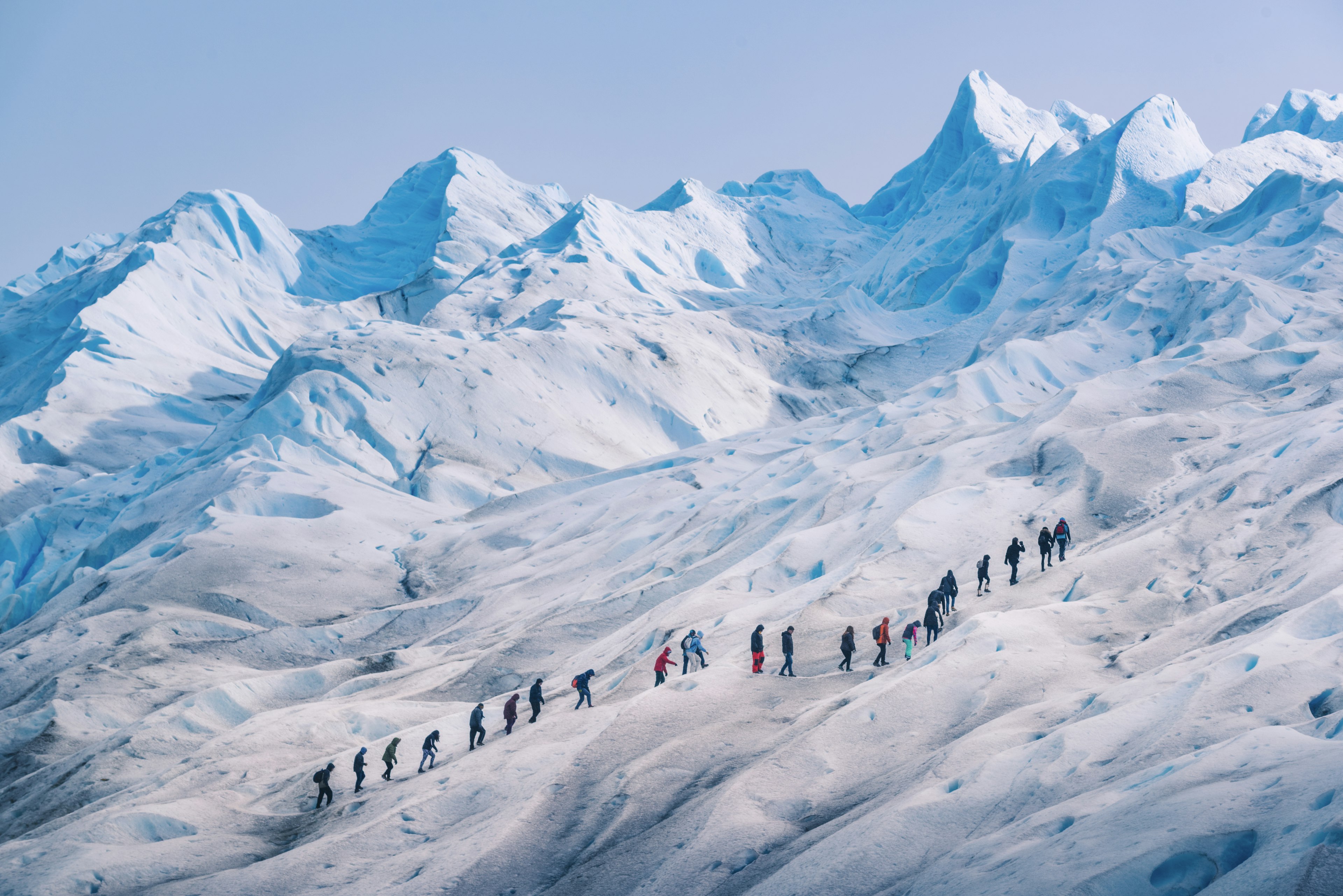 A row of hikers following a trail on a vast glacier