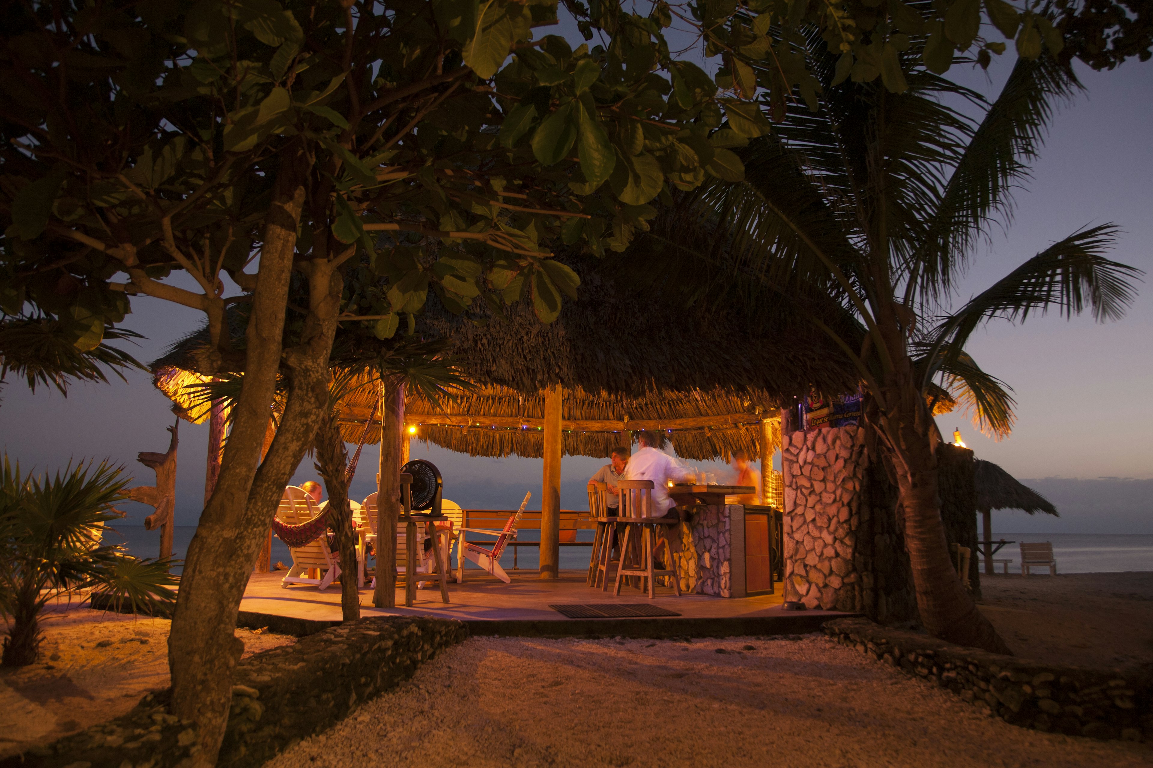 People at a beachside bar in a thatched-roof palapa hut at sunset on Utila, Honduras