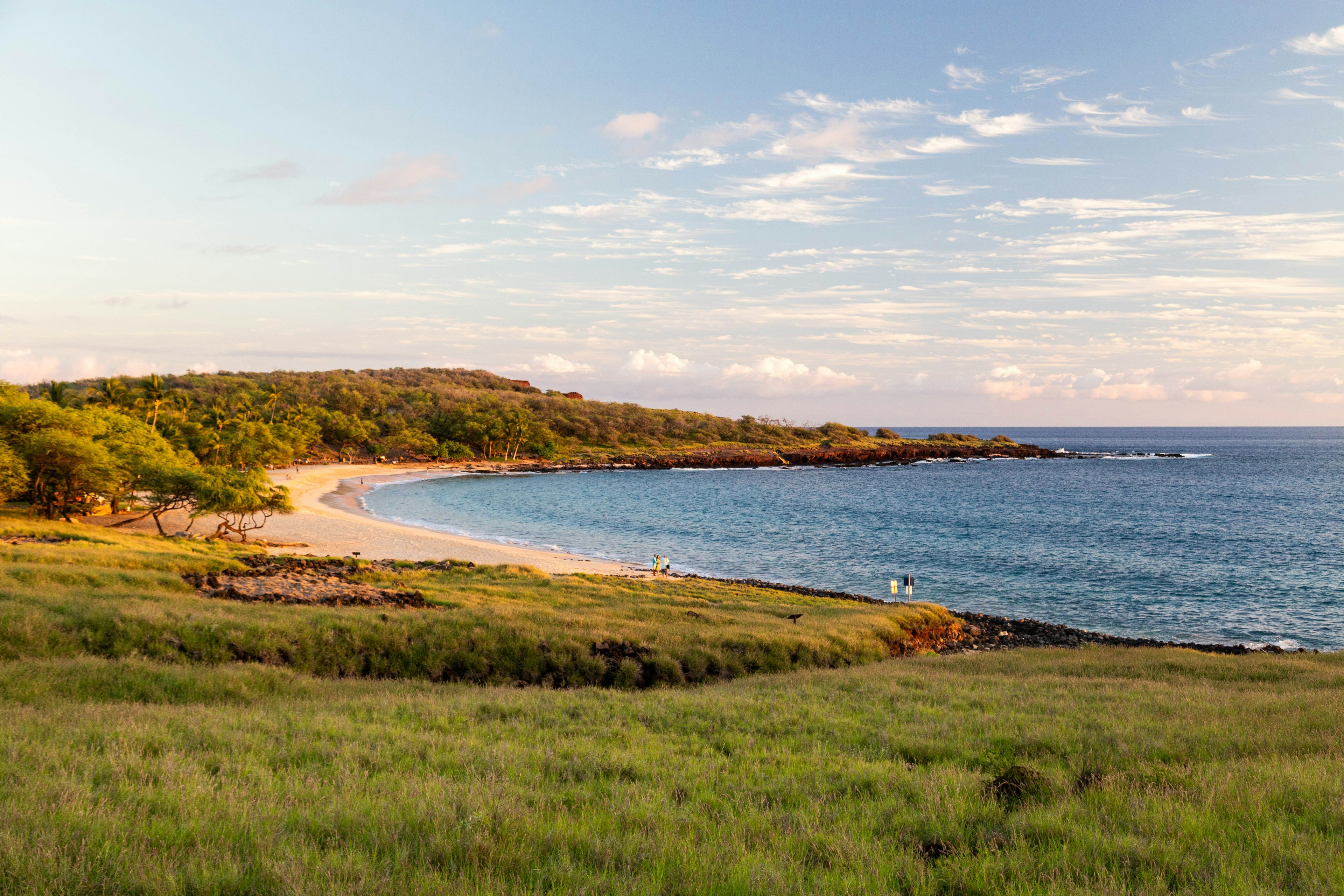 A golden beach at sunset with a few people walking along it