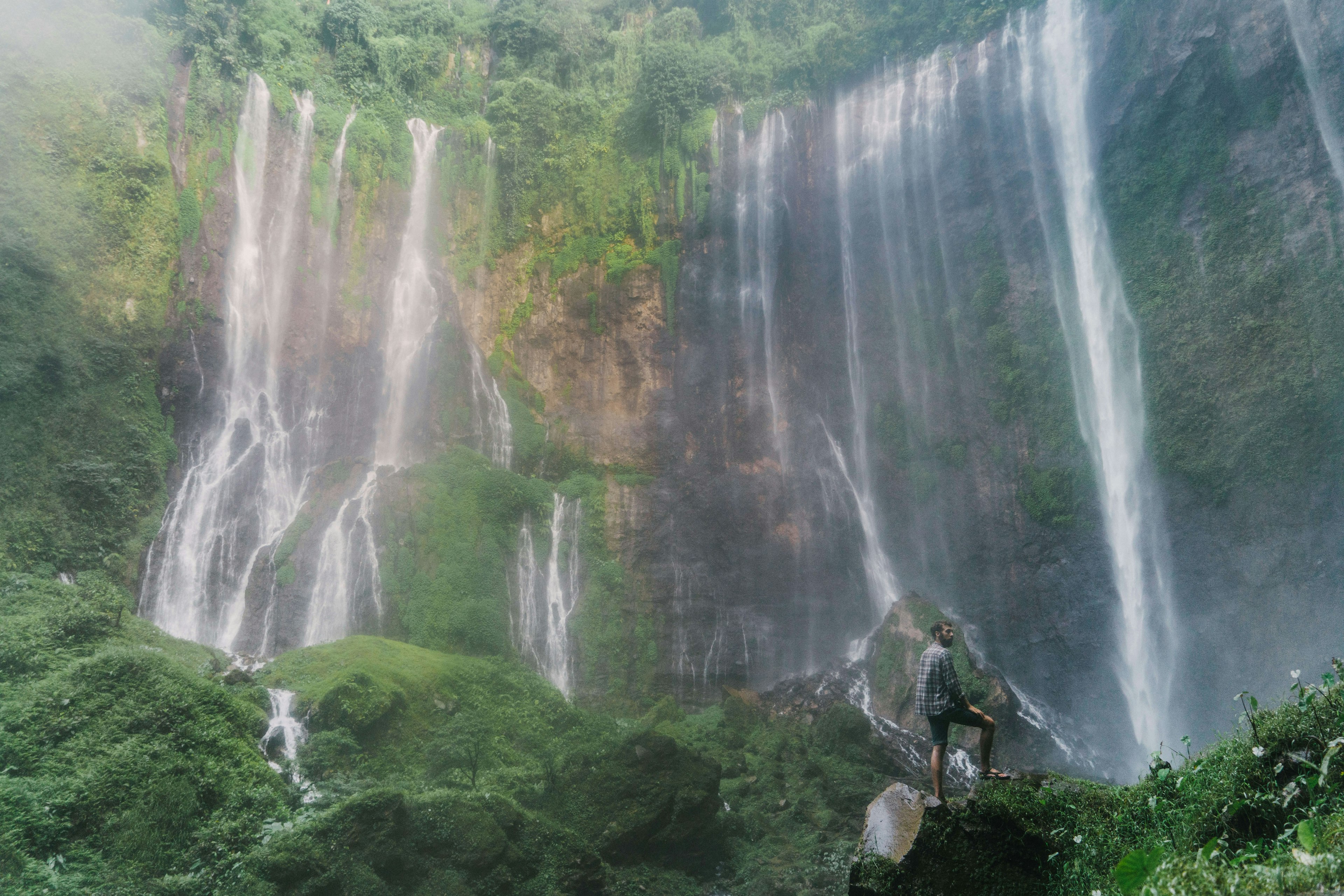 Man standing and looking at Tumpak Sewu waterfall on Java, Indonesia.
