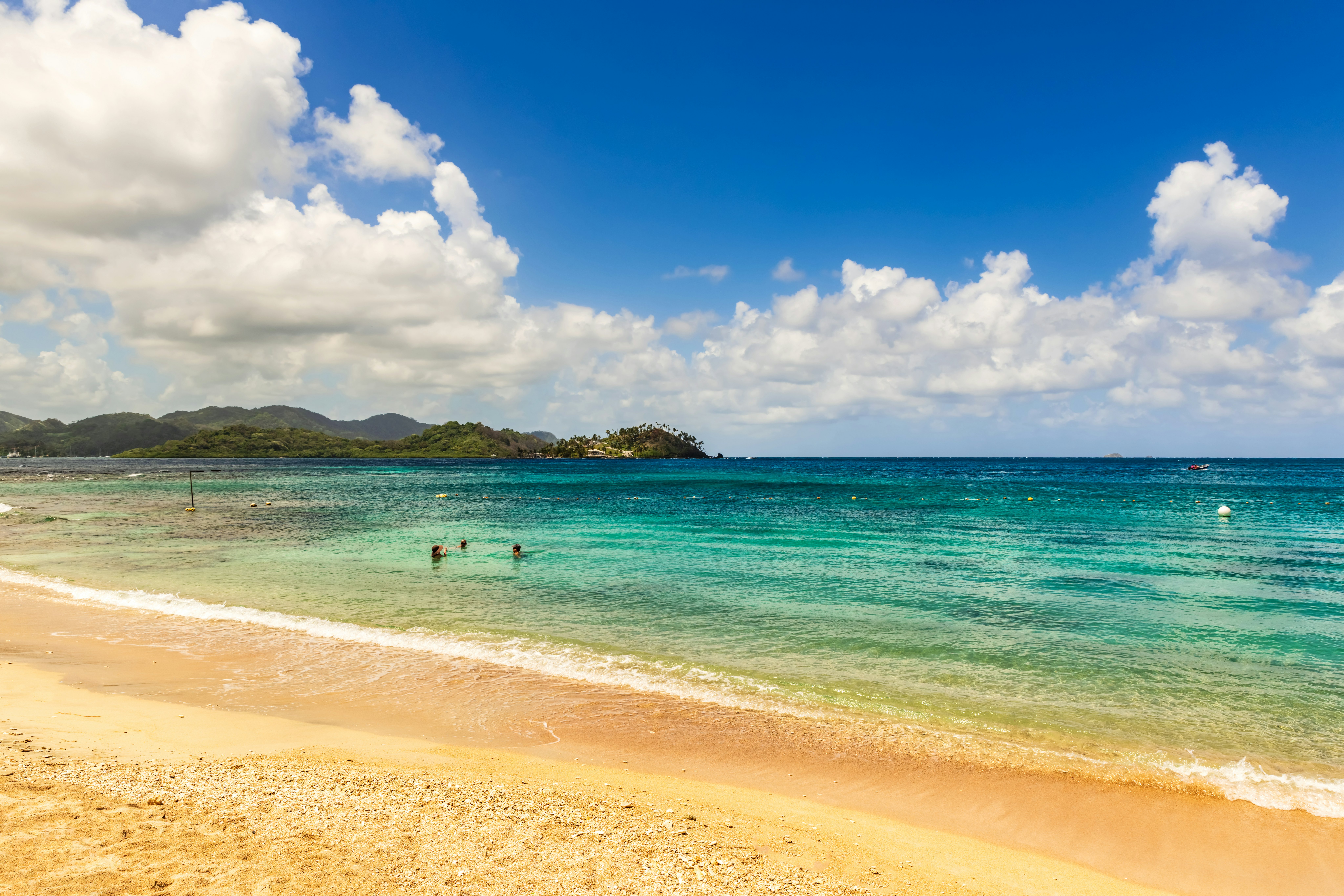 A beach on Isla Grande, Panama. Two people lounge in the shallow turquoise waters near a golden strip of sand.