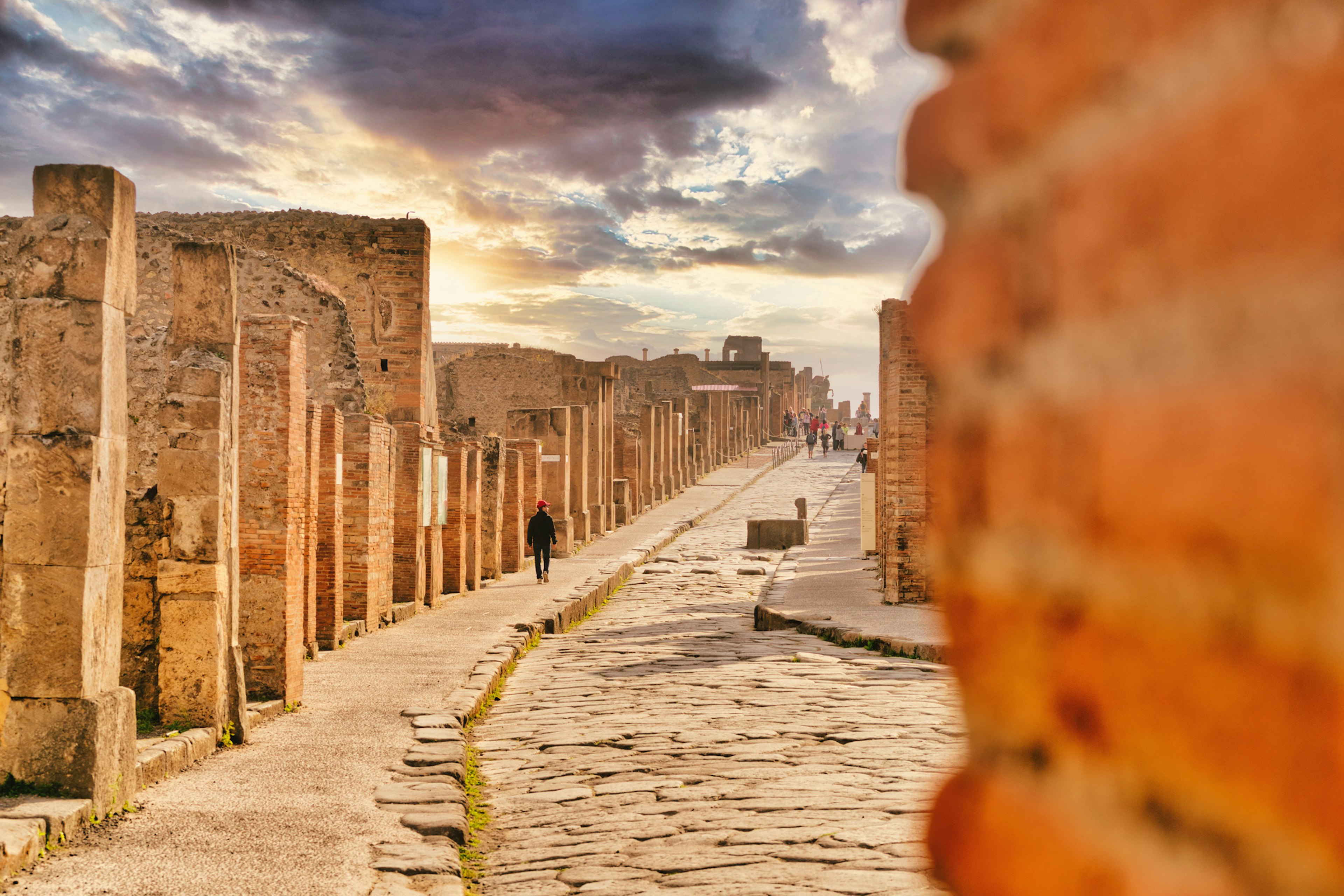 A sole figure walks down an ancient pathway surrounded by ruins