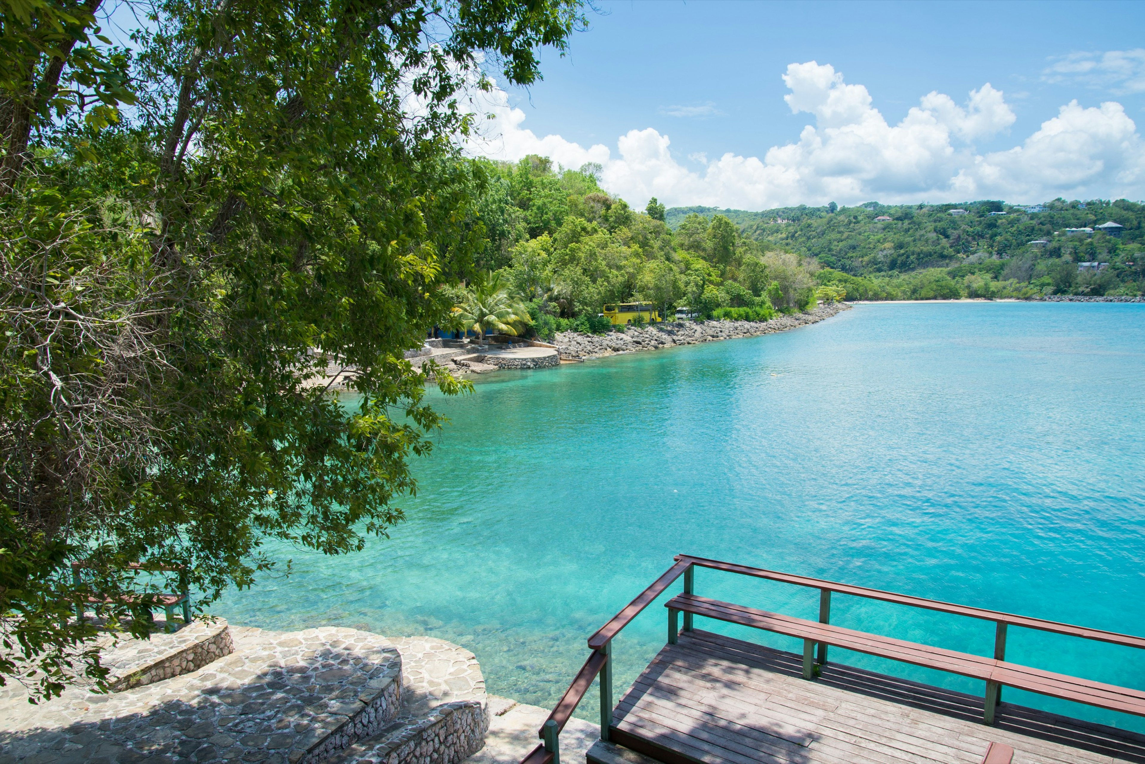 Turquoise water is surrounded by brick structures, rocks and green trees at James Bond Beach