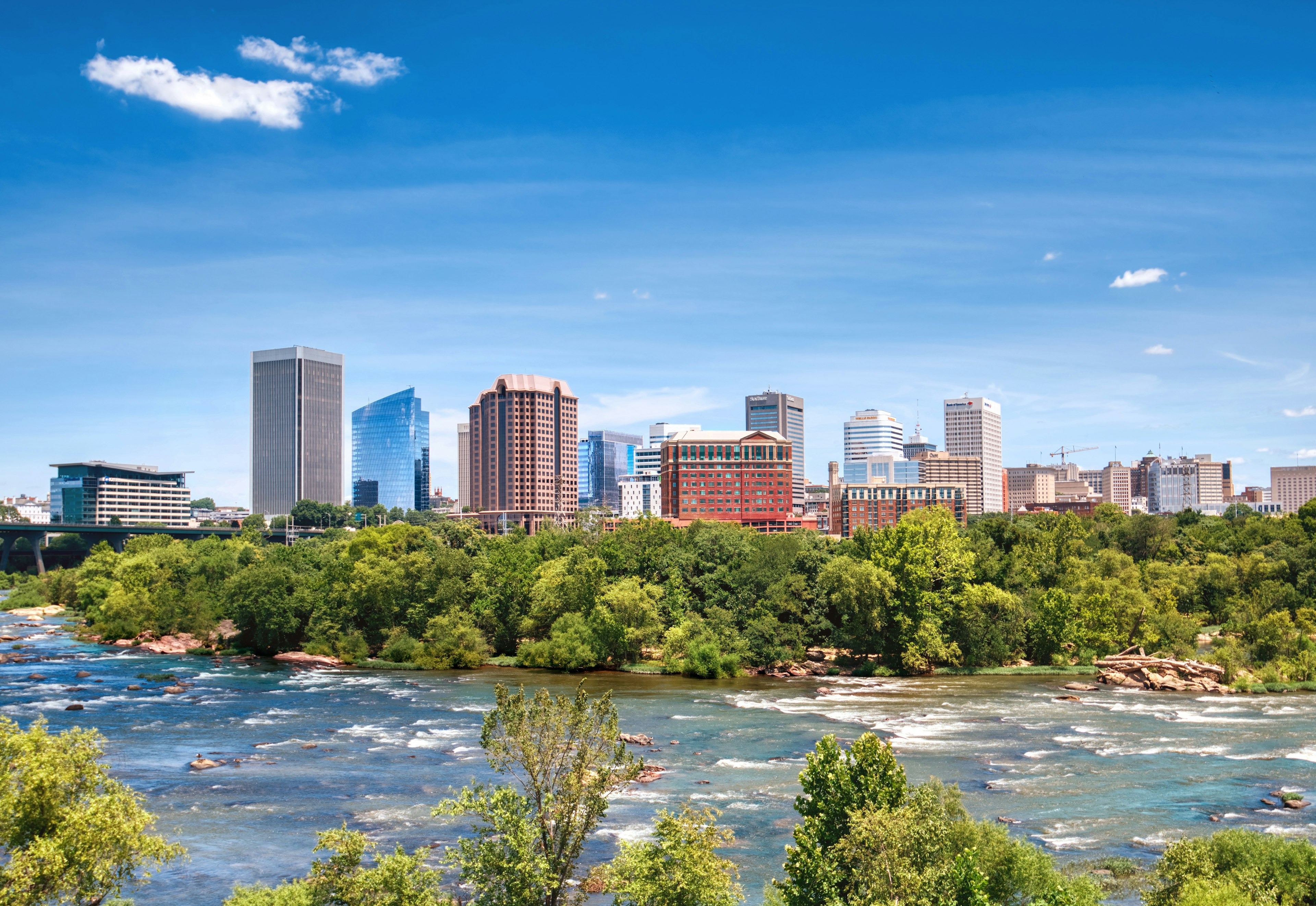 A view of the skyline of Richmond, Virginia, with the wide James River running in front of it.