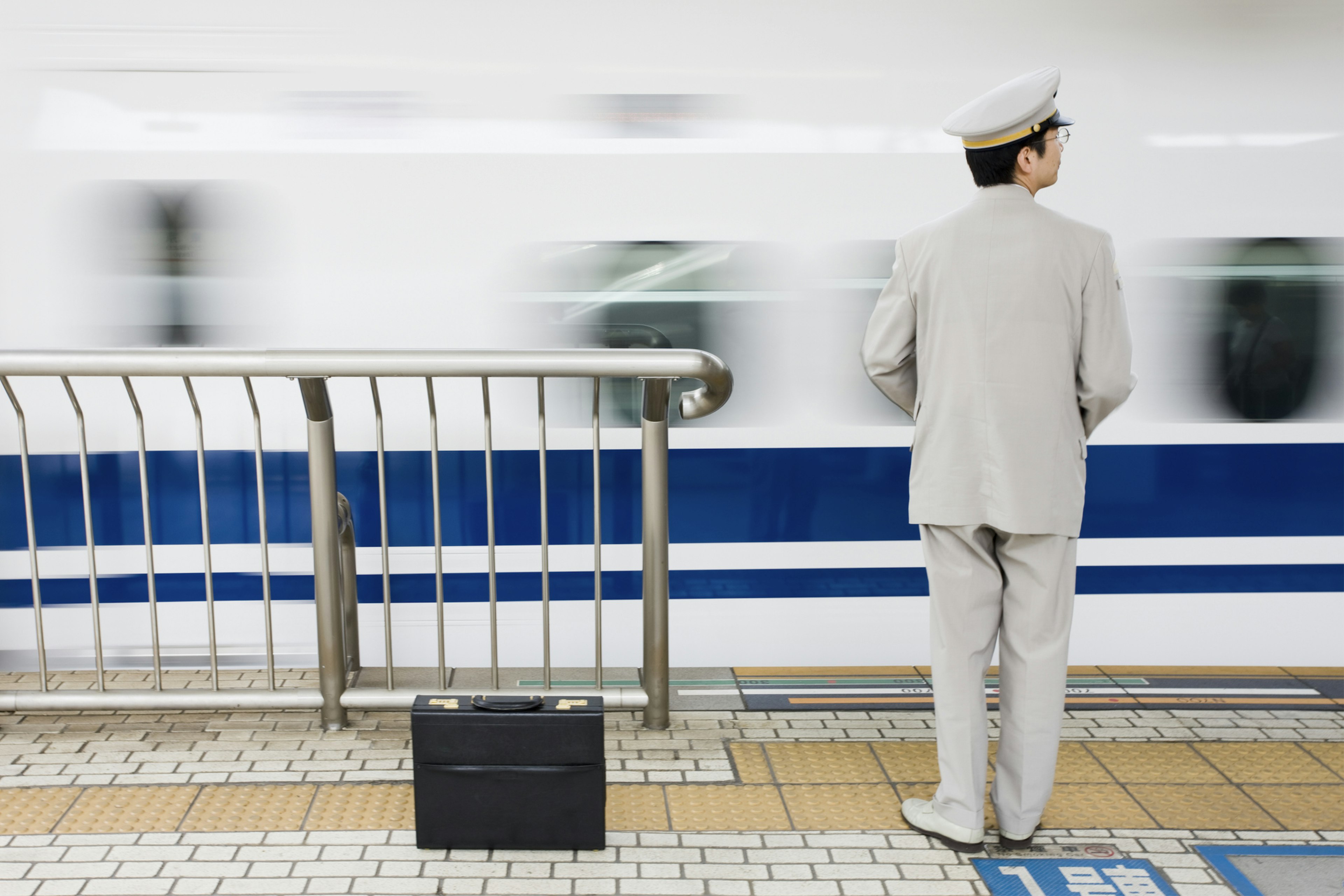 A guard stands on the edge of the platform as a bullet train pulls in